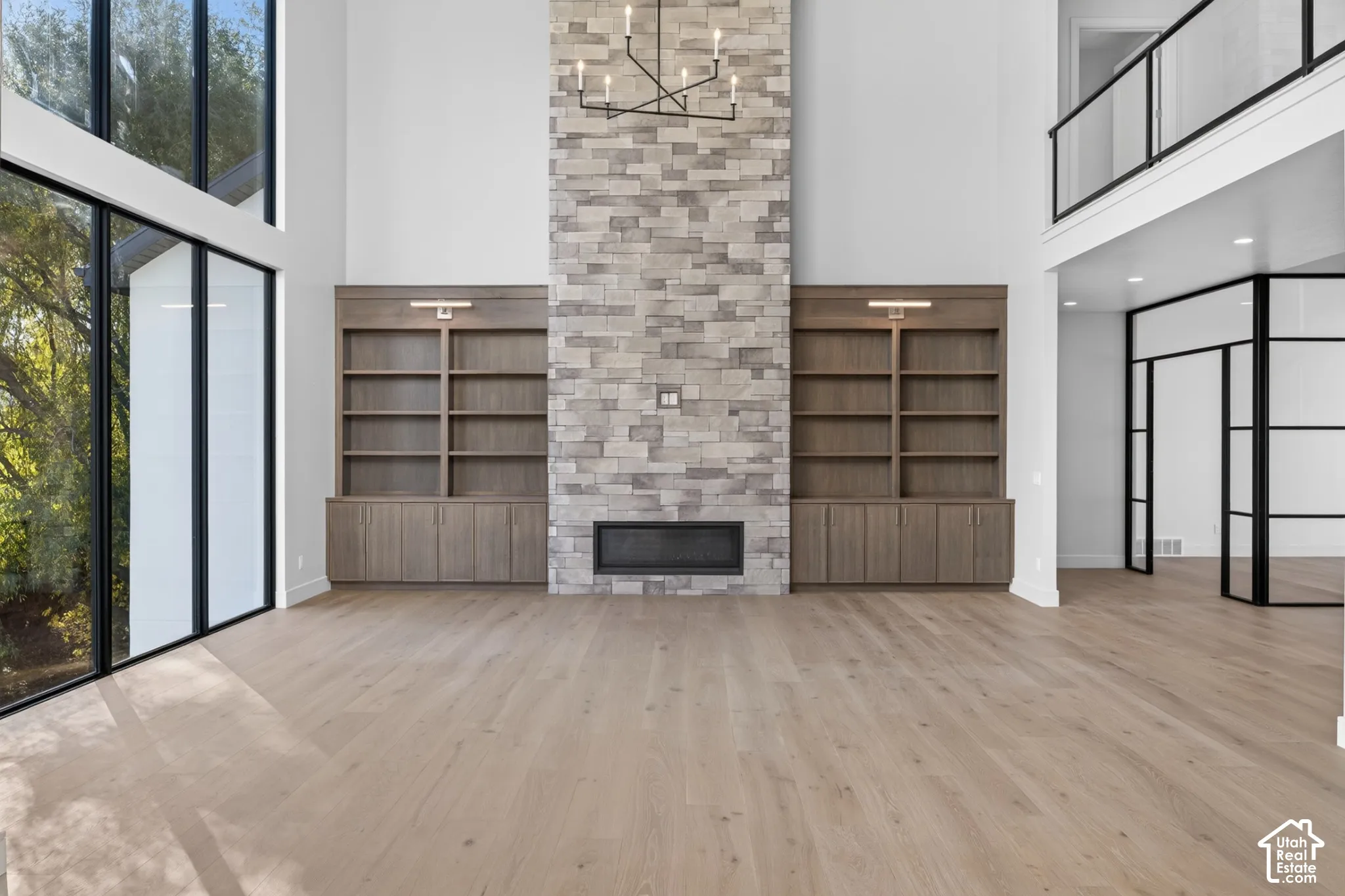 Double-height ceilings, floor-to-ceiling stone fireplace, custom wood-finish built-in cabinetry, wood-finish flooring, and black-frame glass accents