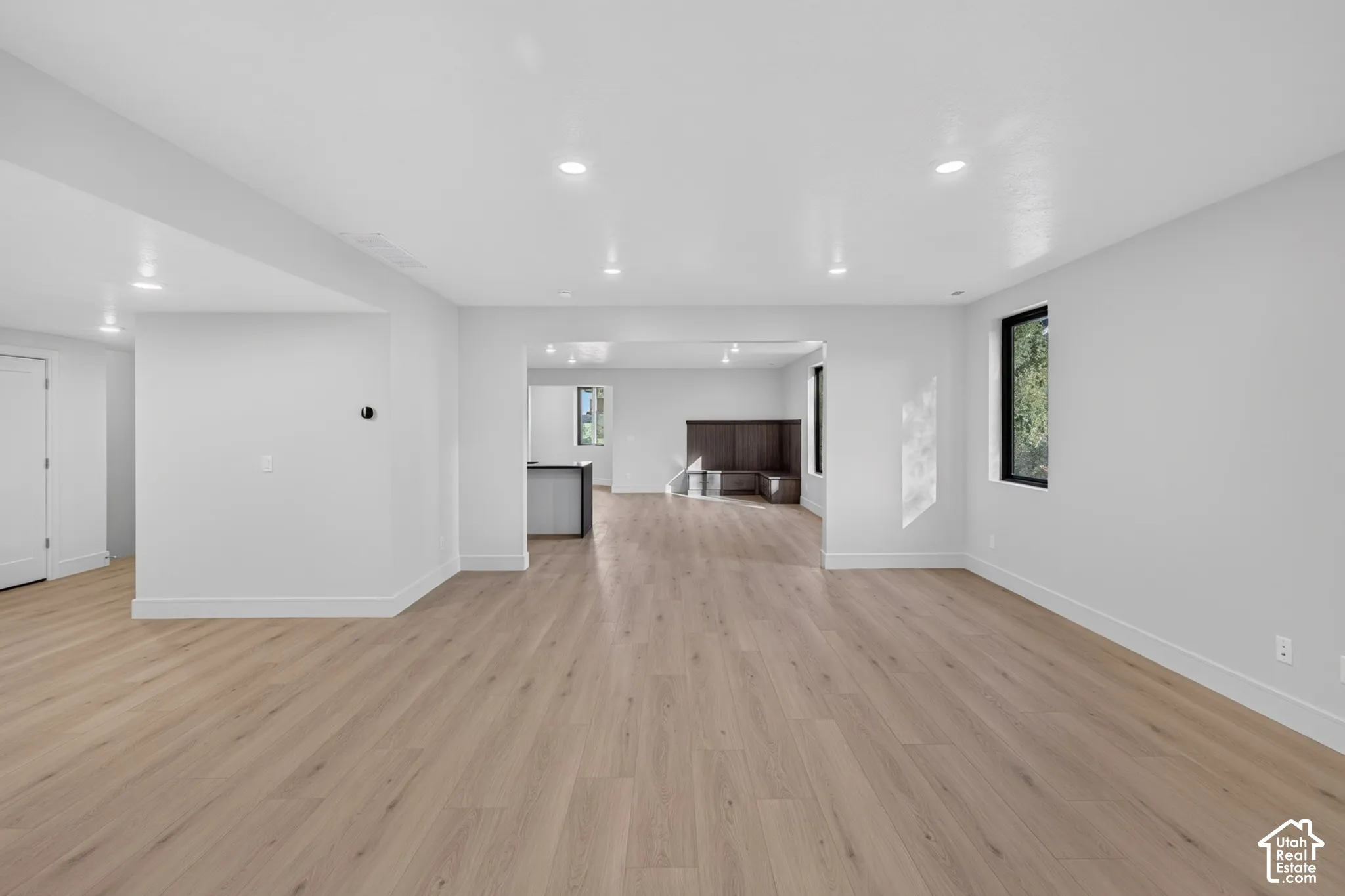 Open-concept interior featuring light wood-finish flooring, recessed lighting, and large windows with black frames