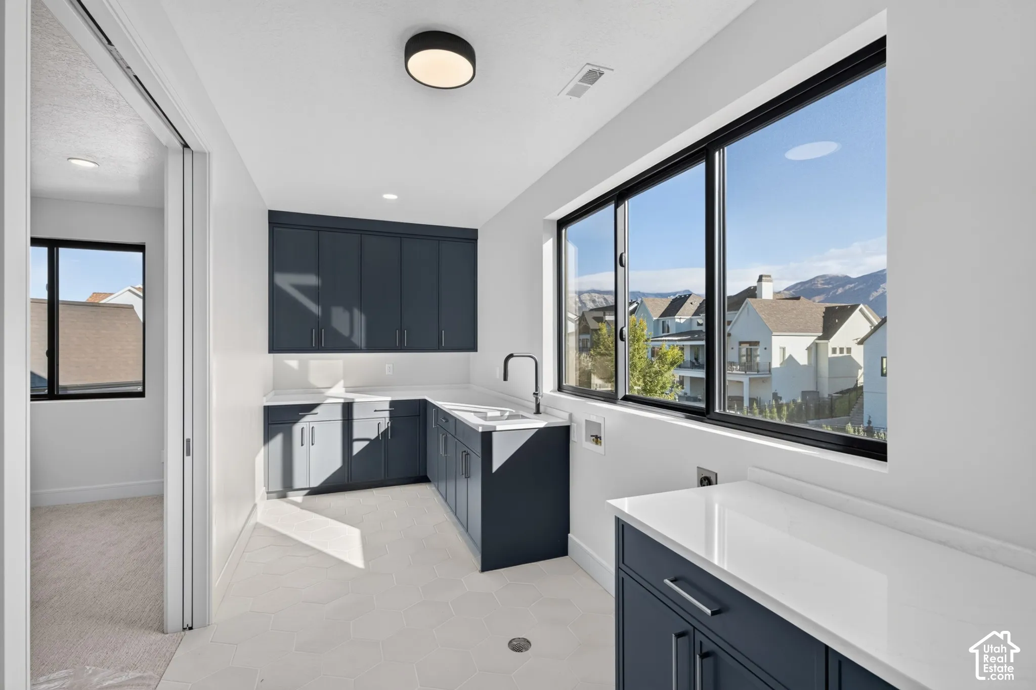 Dark-toned cabinetry featuring matte finish hardware, stone-composite countertops, hexagon tile flooring, a deep-basin sink with a matte black faucet, and expansive windows