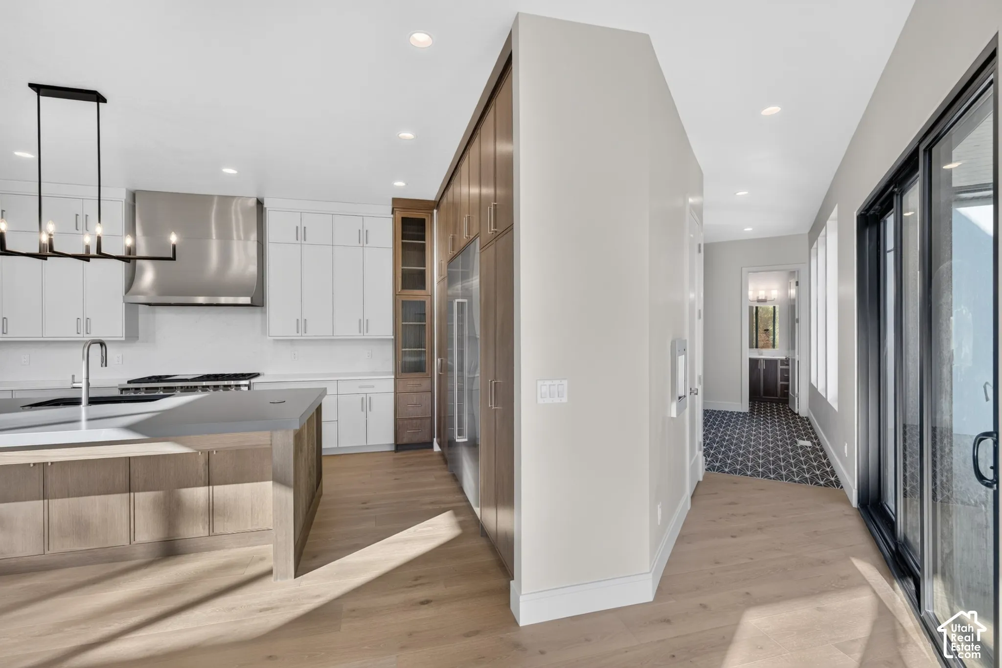 Kitchen featuring wood-finish flooring, two-tone cabinetry, a stainless steel range hood, stone-topped island, and sliding glass doors