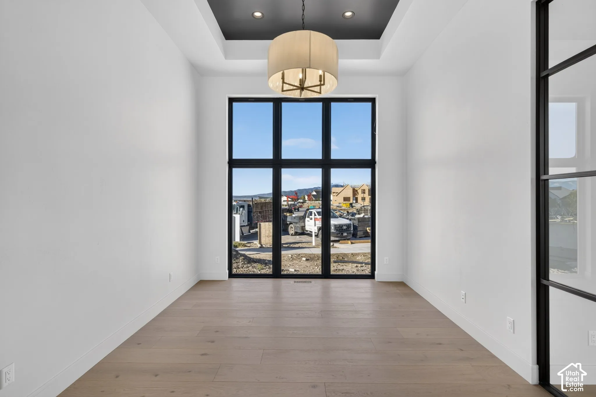 Entryway featuring wood-finish flooring, a tray ceiling with recessed lighting, a statement drum chandelier, floor-to-ceiling windows with black mullions, and a black-framed glass panel wall