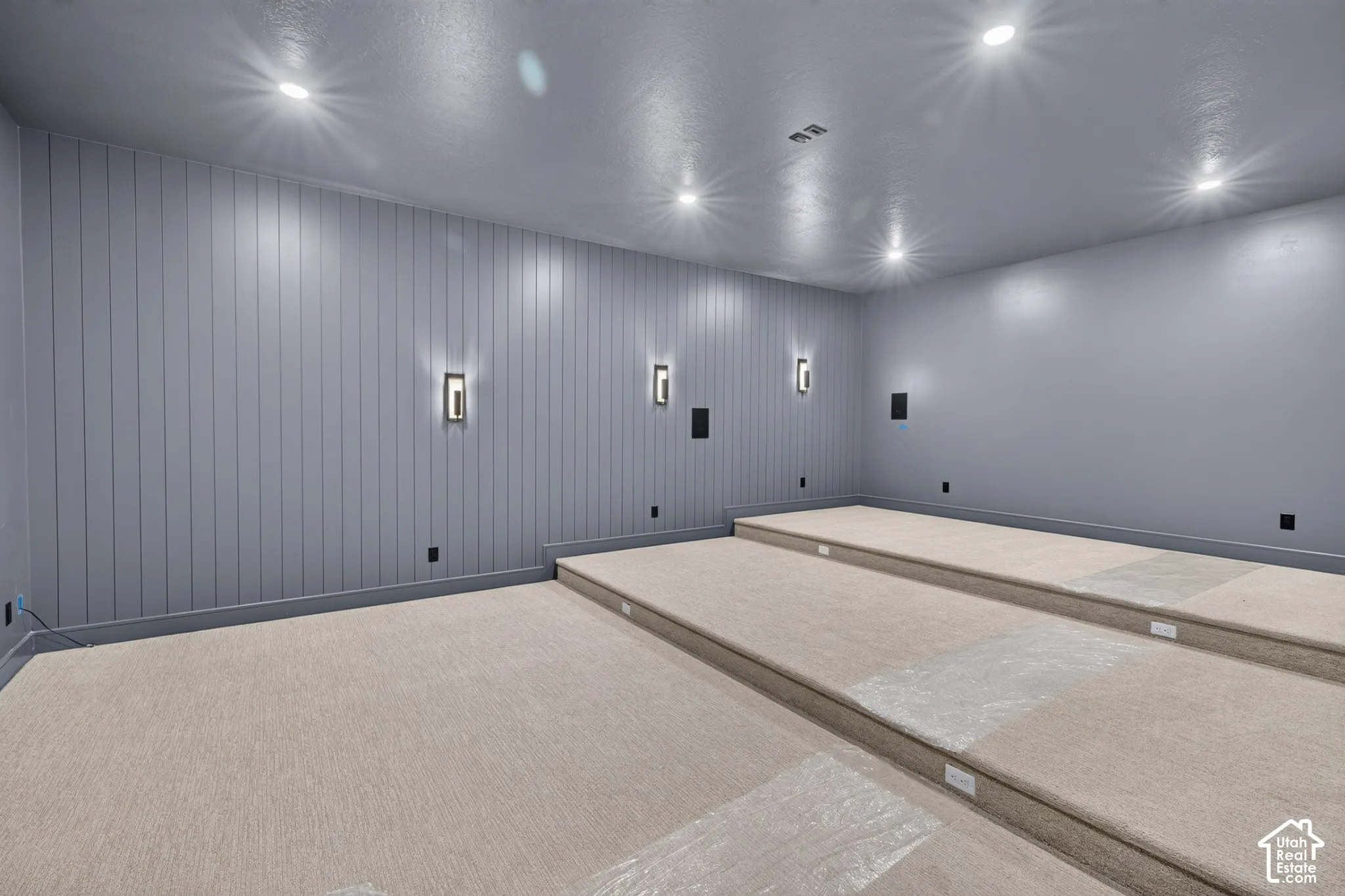 Multi-level tiered flooring, vertical shiplap wall paneling, recessed ceiling lighting, and built-in wall-mounted light fixtures
