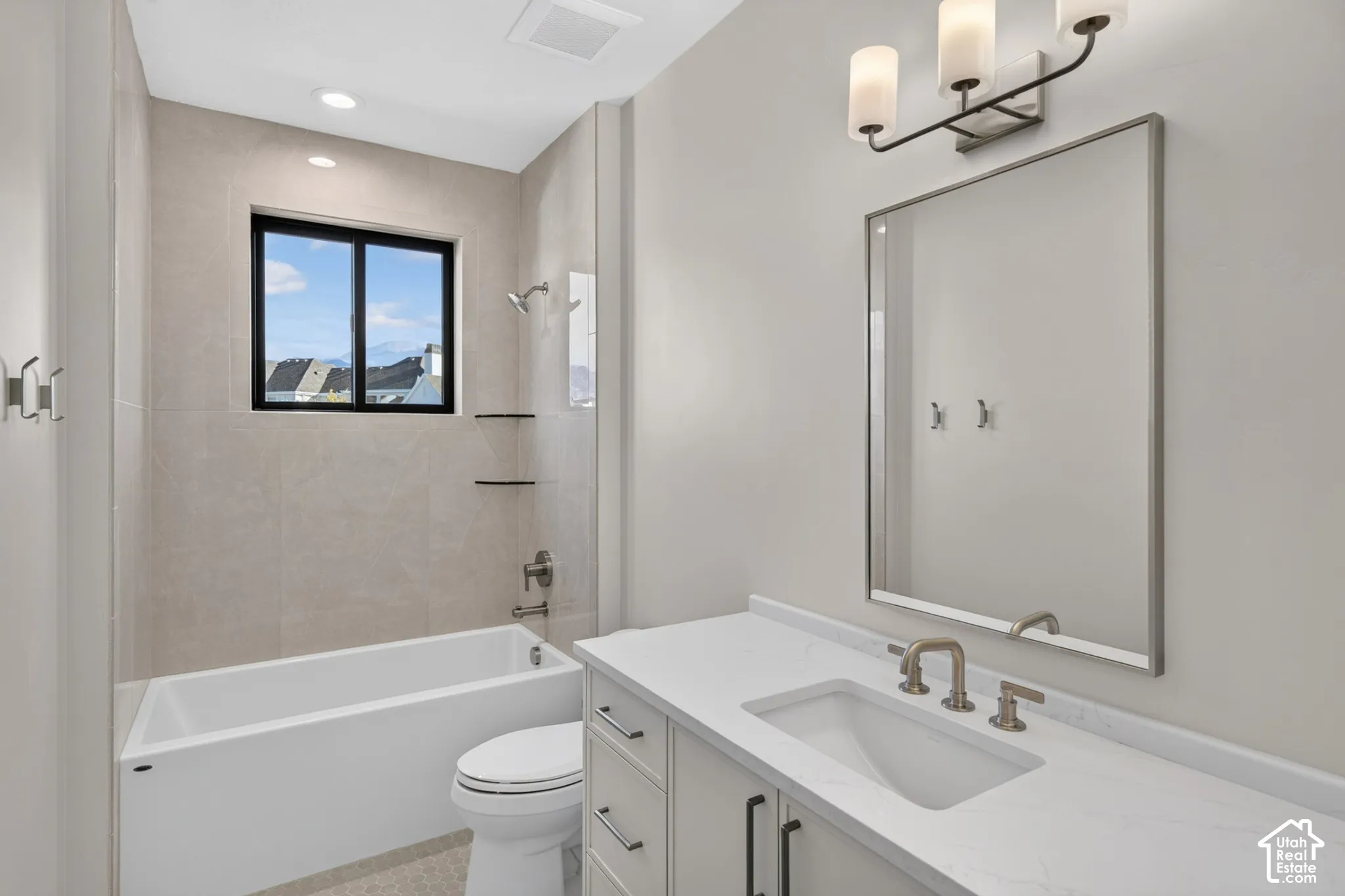 Bathroom featuring a vanity with white stone-finish countertop, undermount sink, three-light fixture, framed mirror, and a tub-shower combination with floor-to-ceiling tile surround