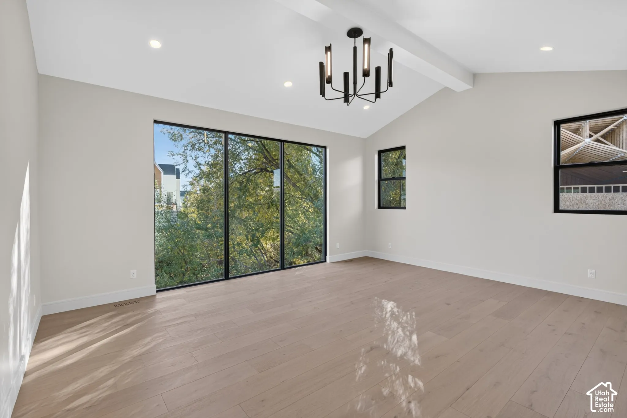 Vaulted ceilings, wood-finish flooring, floor-to-ceiling windows with black frames, and a modern multi-arm chandelier