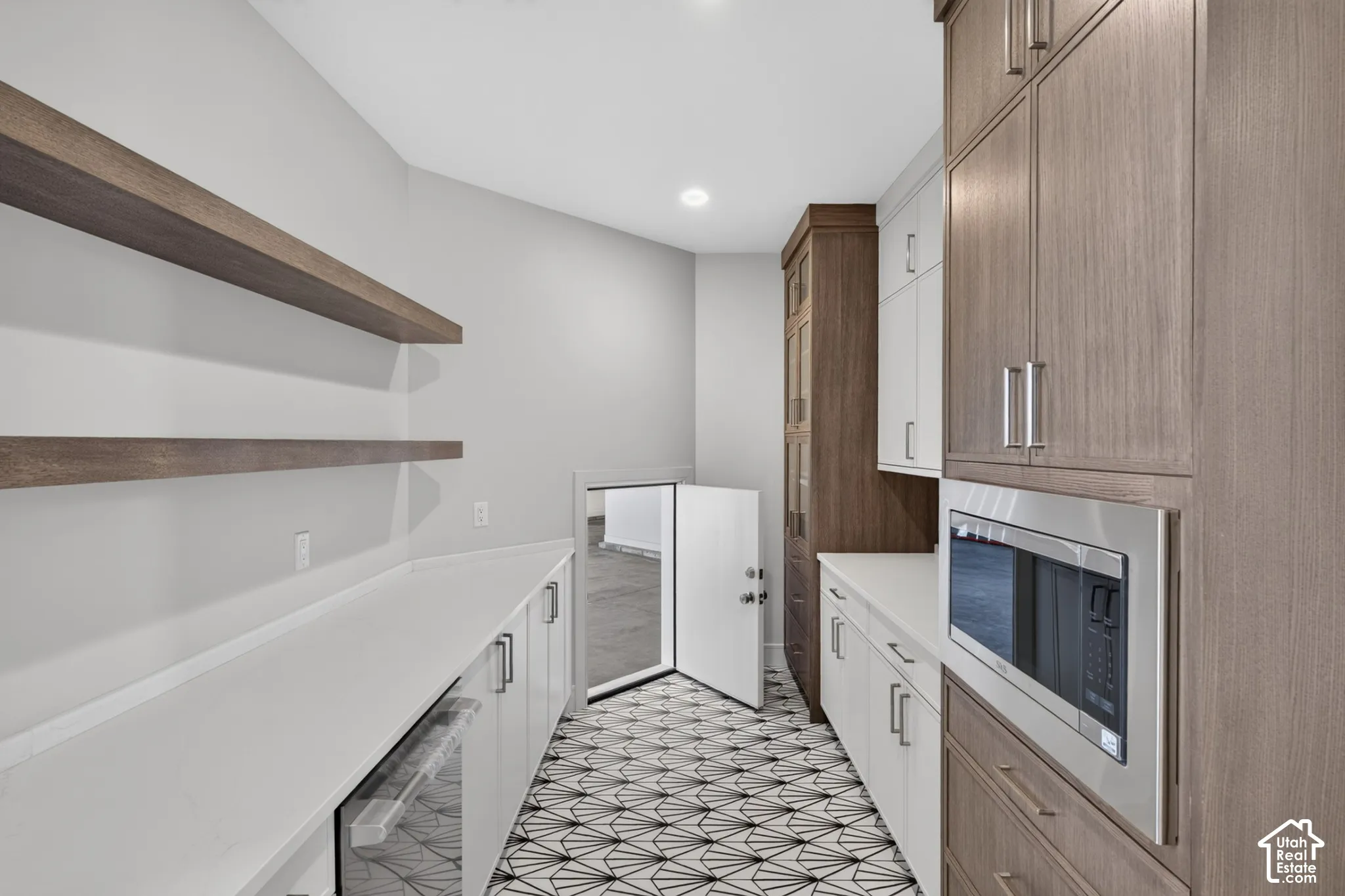 Butler's pantry featuring two-tone cabinetry, quartz countertops, floating wood shelves, geometric tile flooring, and a built-in microwave