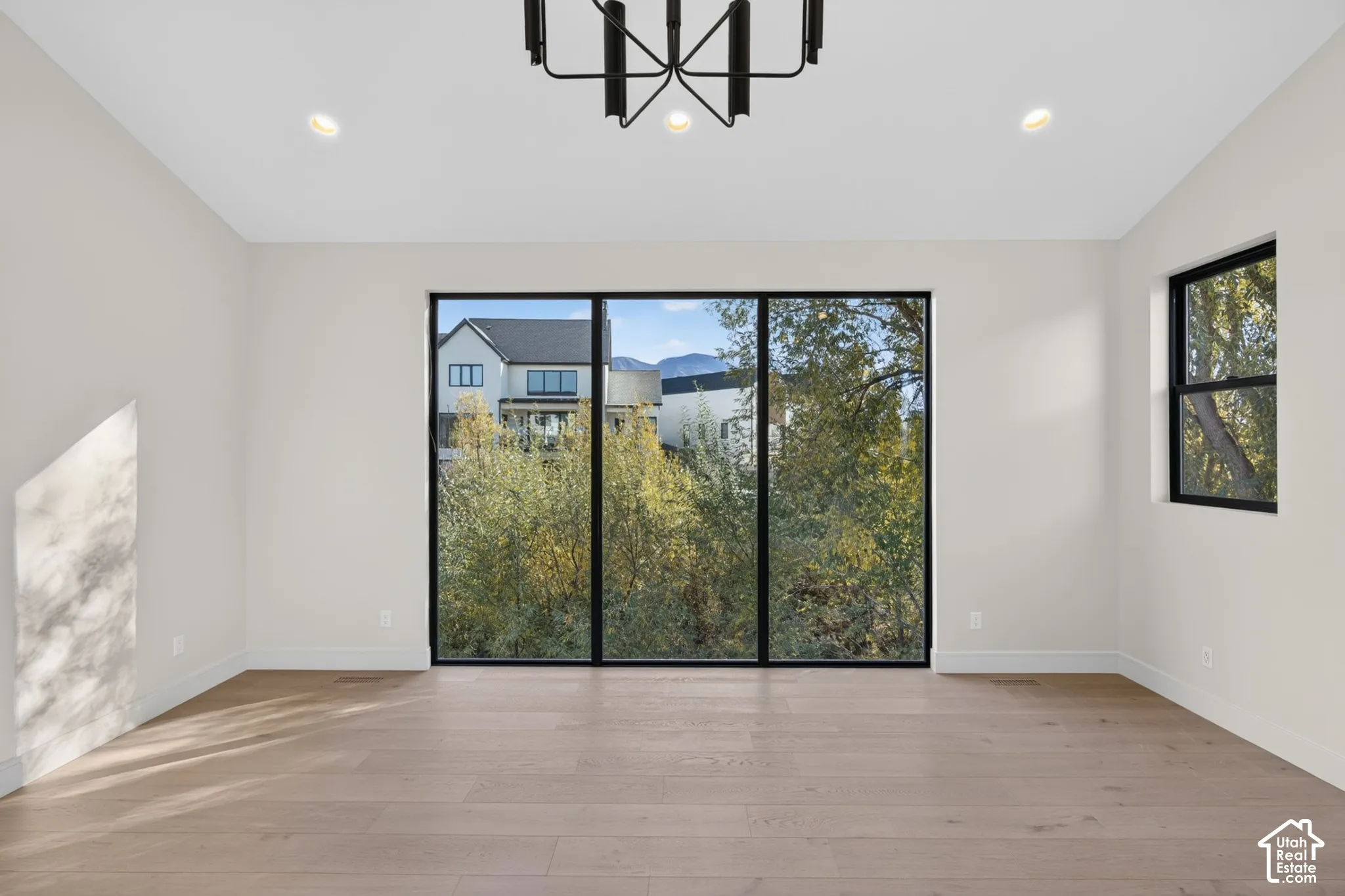 Expansive room featuring floor-to-ceiling windows with black frames, wood-finish flooring, recessed lighting, and a modern tiered chandelier