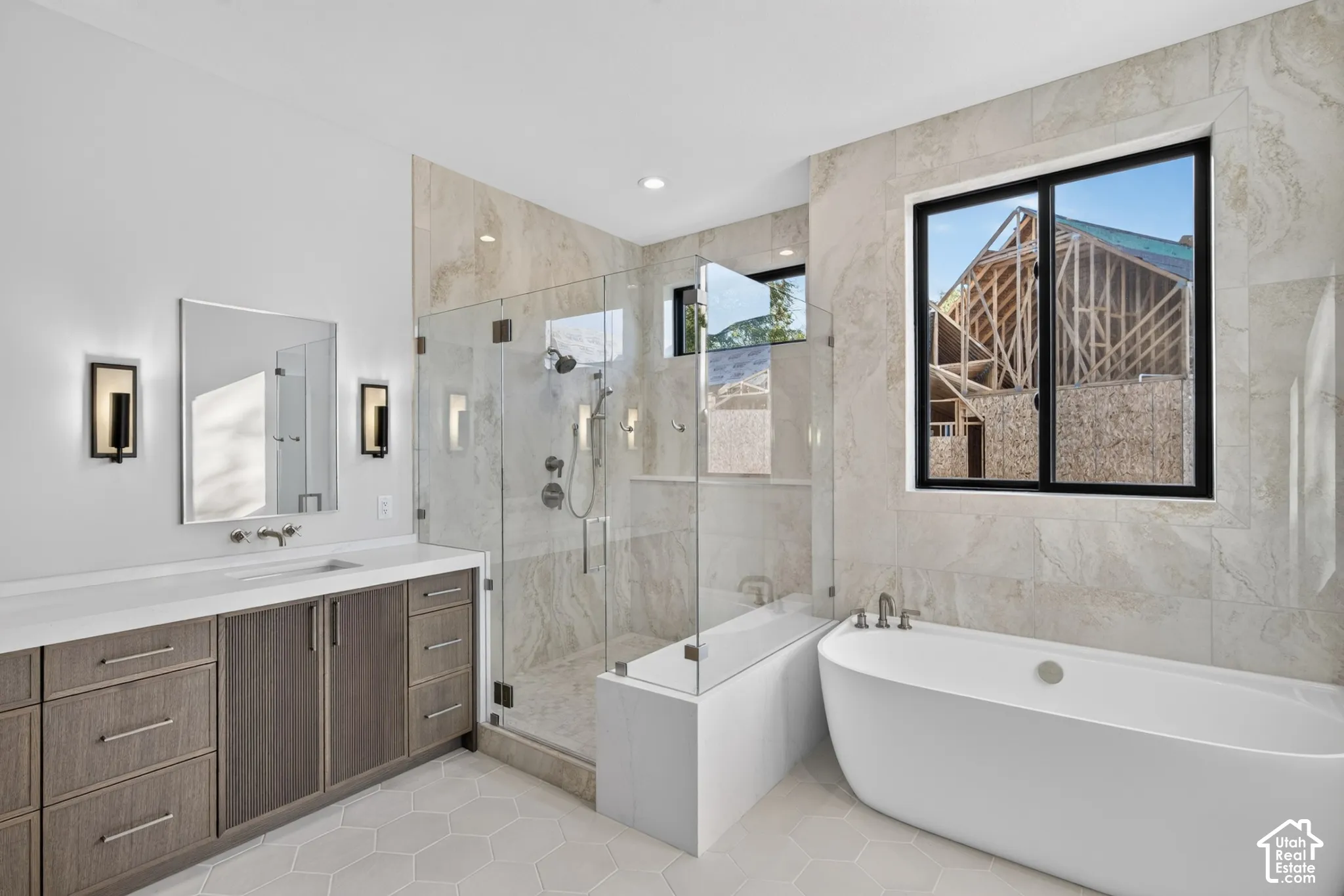 Bathroom featuring a wood-finish vanity with a light countertop, a freestanding soaking tub, a walk-in glass-enclosed shower with tile surround, and hexagonal tile flooring