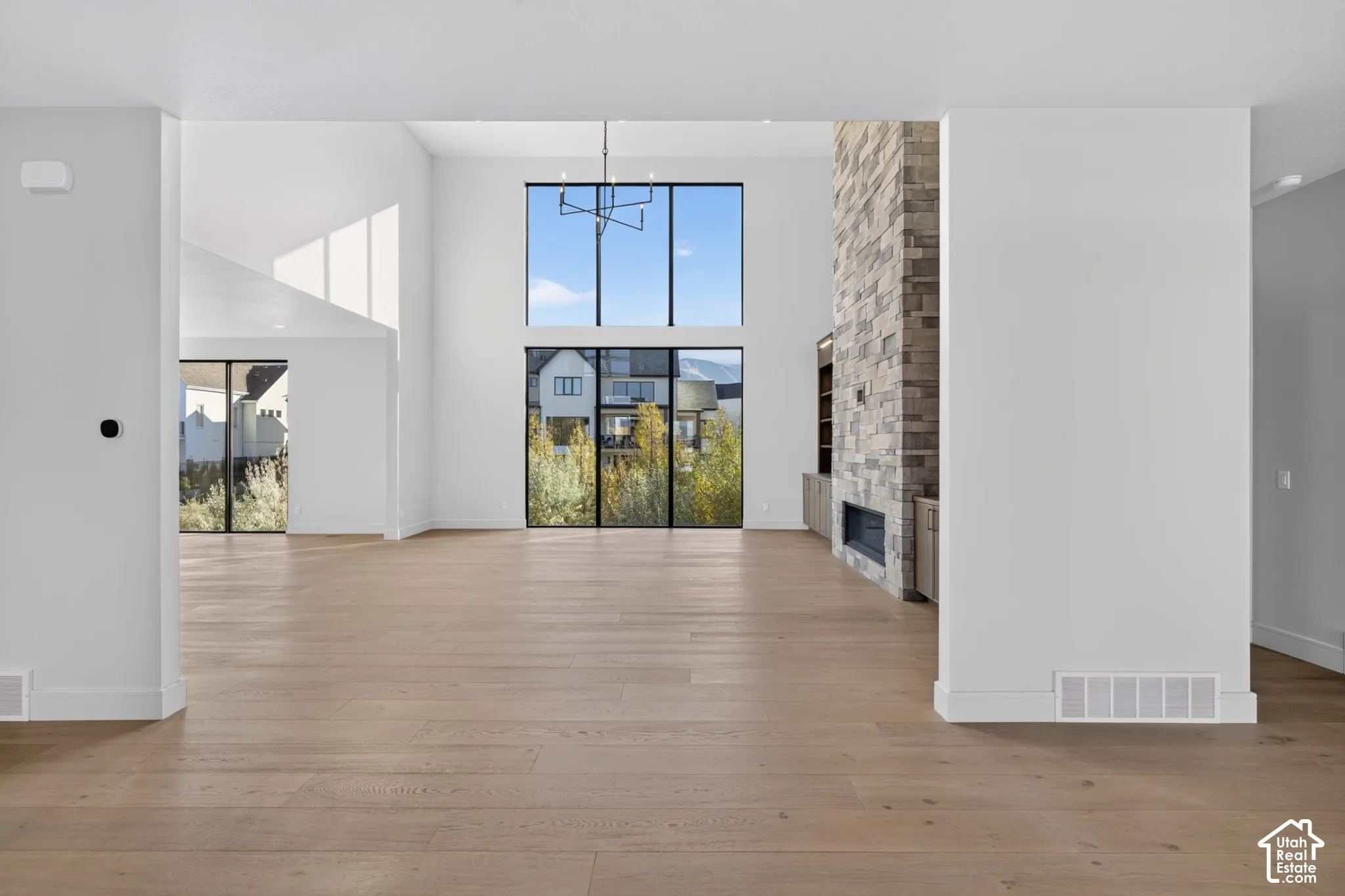 Open-concept interior featuring wood-finish flooring, floor-to-ceiling windows, a full-height stone fireplace surround, and a modern tiered chandelier
