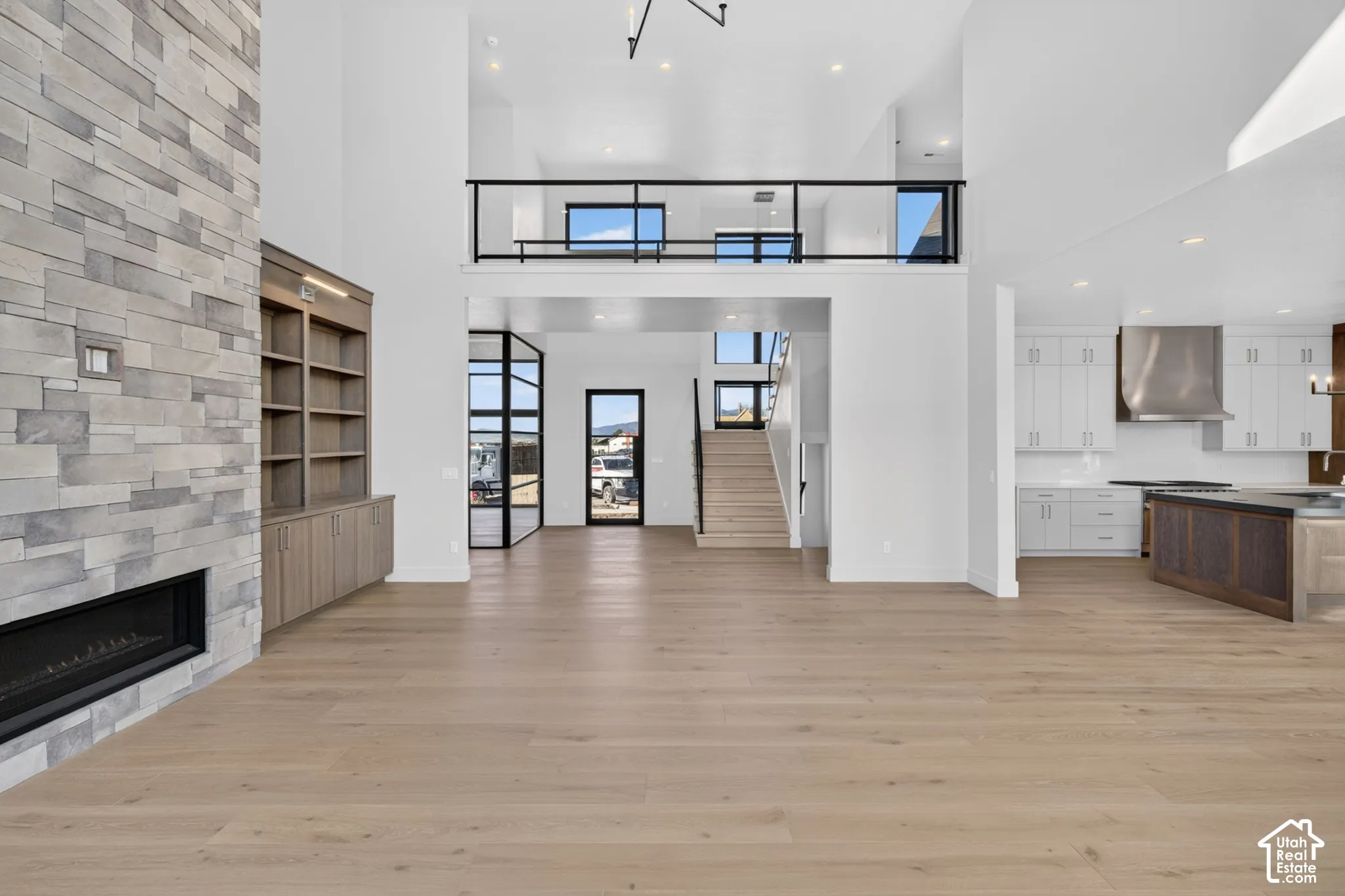 Open-concept interior featuring floor-to-ceiling dry-stack stone fireplace, wood-finish flooring, built-in cabinetry, custom metal stair railing, and high ceilings