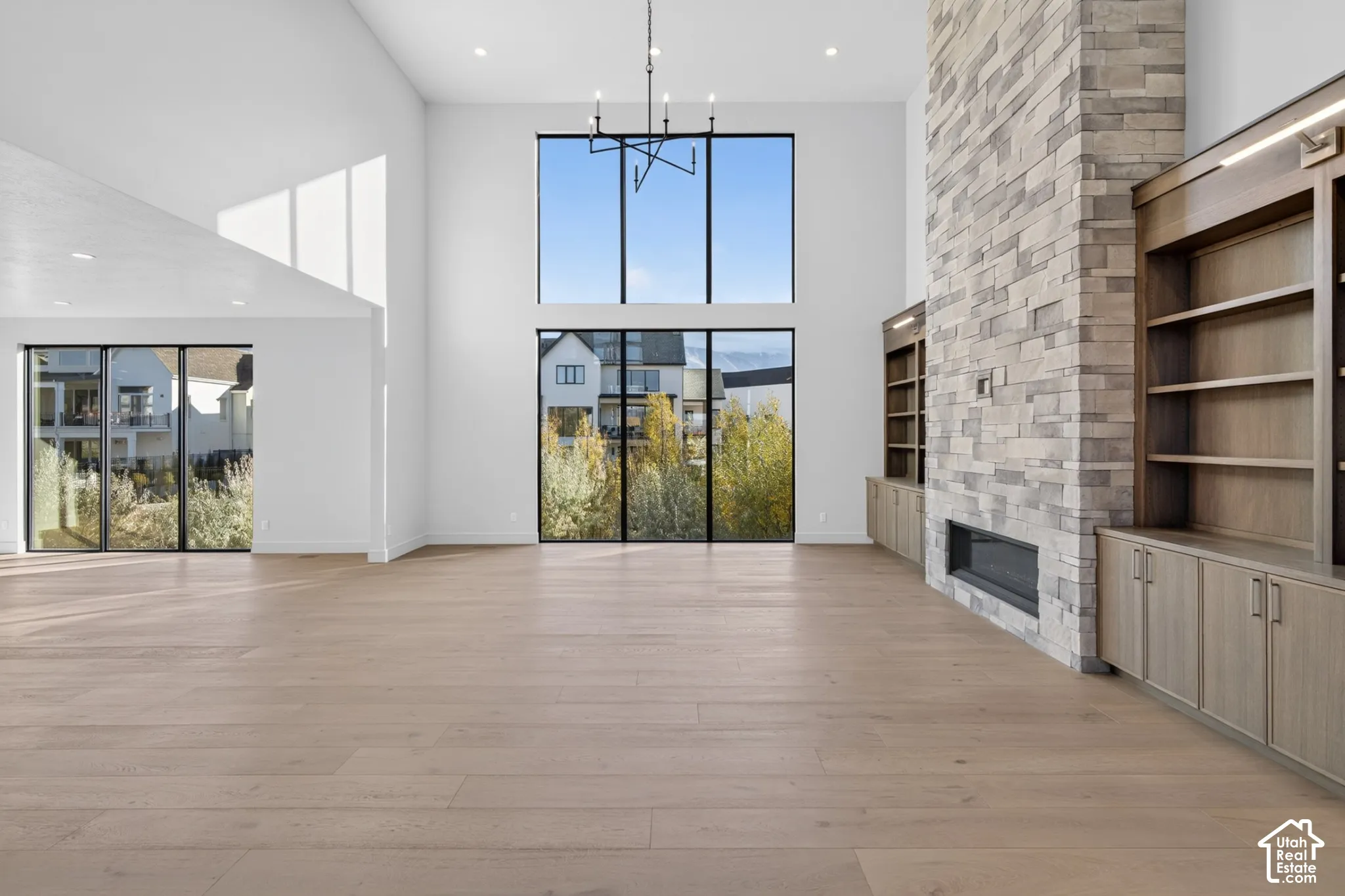 Double-height ceiling, floor-to-ceiling windows with black framing, floor-to-ceiling stone fireplace, custom built-in wood cabinetry, and wood-finish flooring