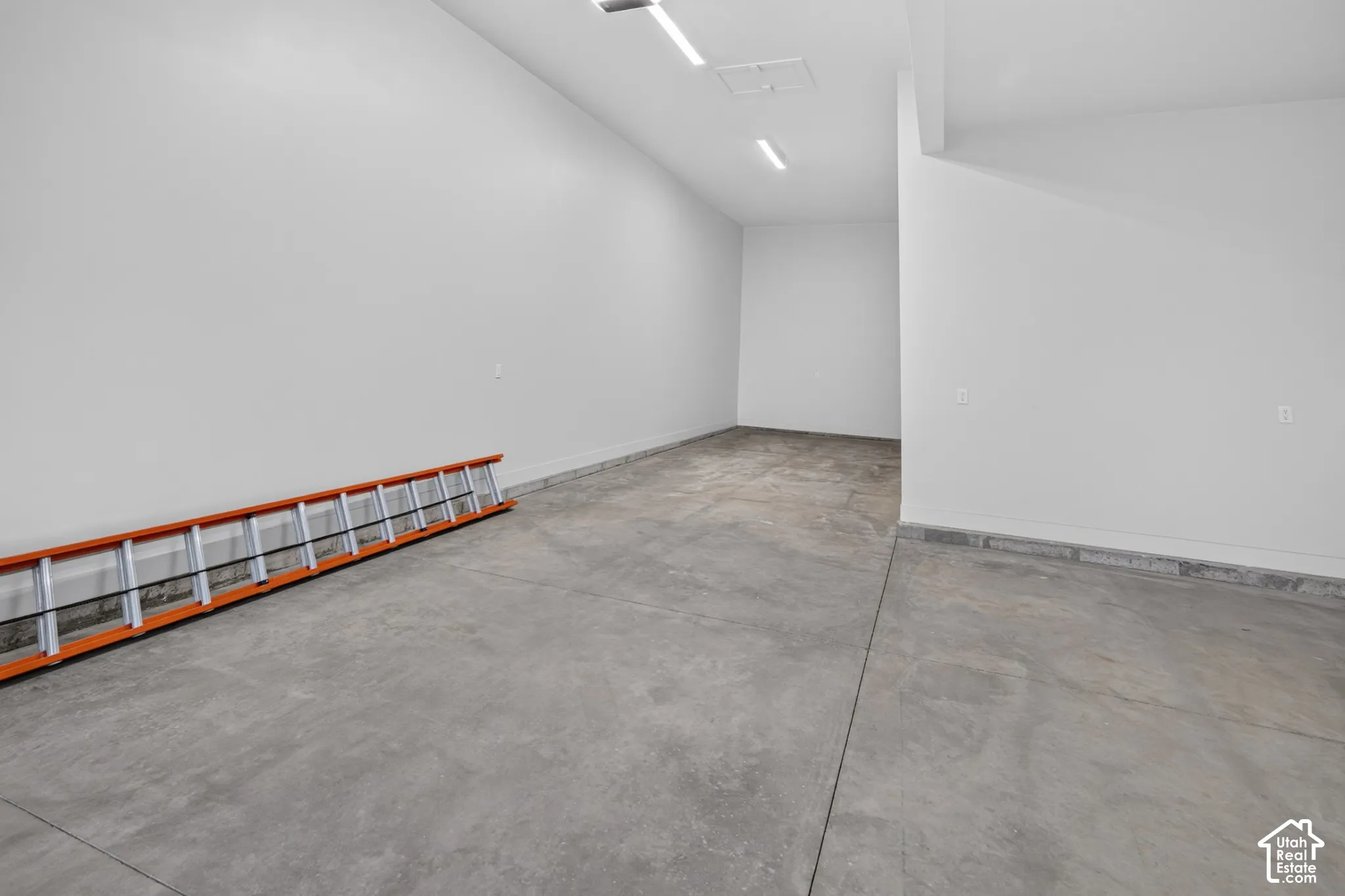 Finished garage space featuring vaulted ceilings, smooth concrete flooring, and ceiling-mounted LED lighting