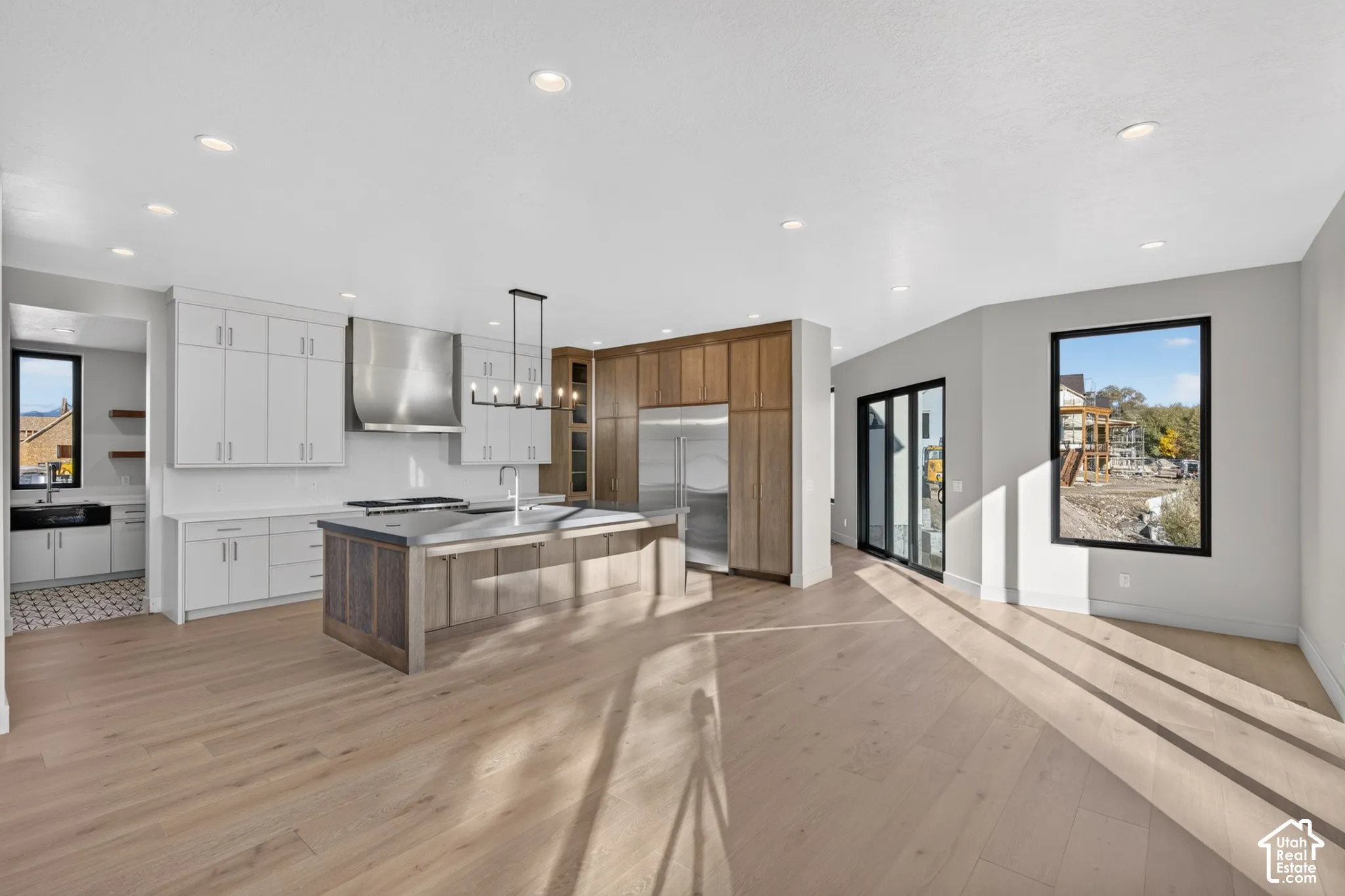 Kitchen featuring wood-finish flooring, dual-tone cabinetry, stainless steel range hood, center island with stone countertop, and recessed lighting