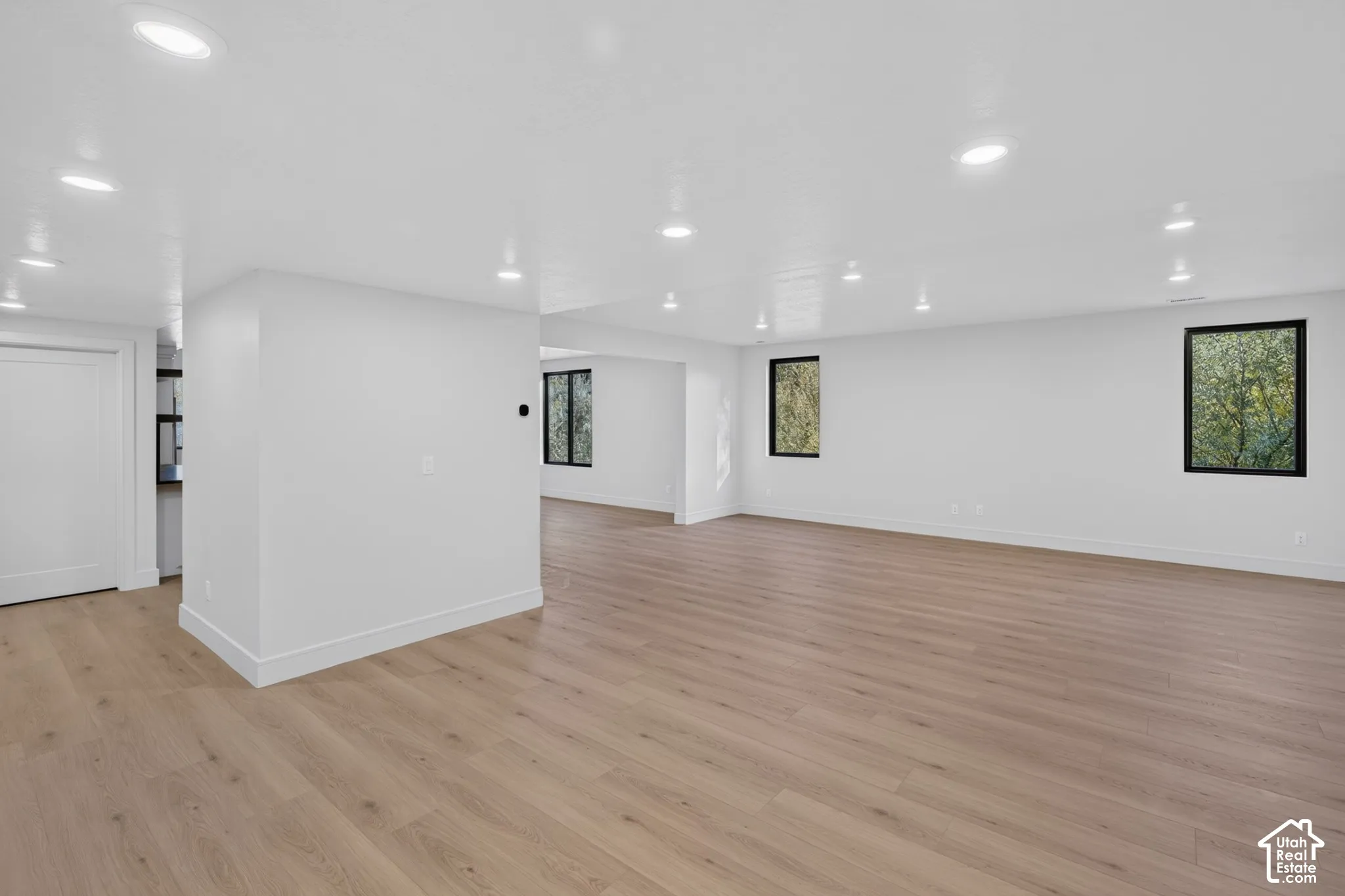 Open-concept interior featuring light wood-finish flooring, recessed lighting, smooth wall finishes, and multiple windows with black trim