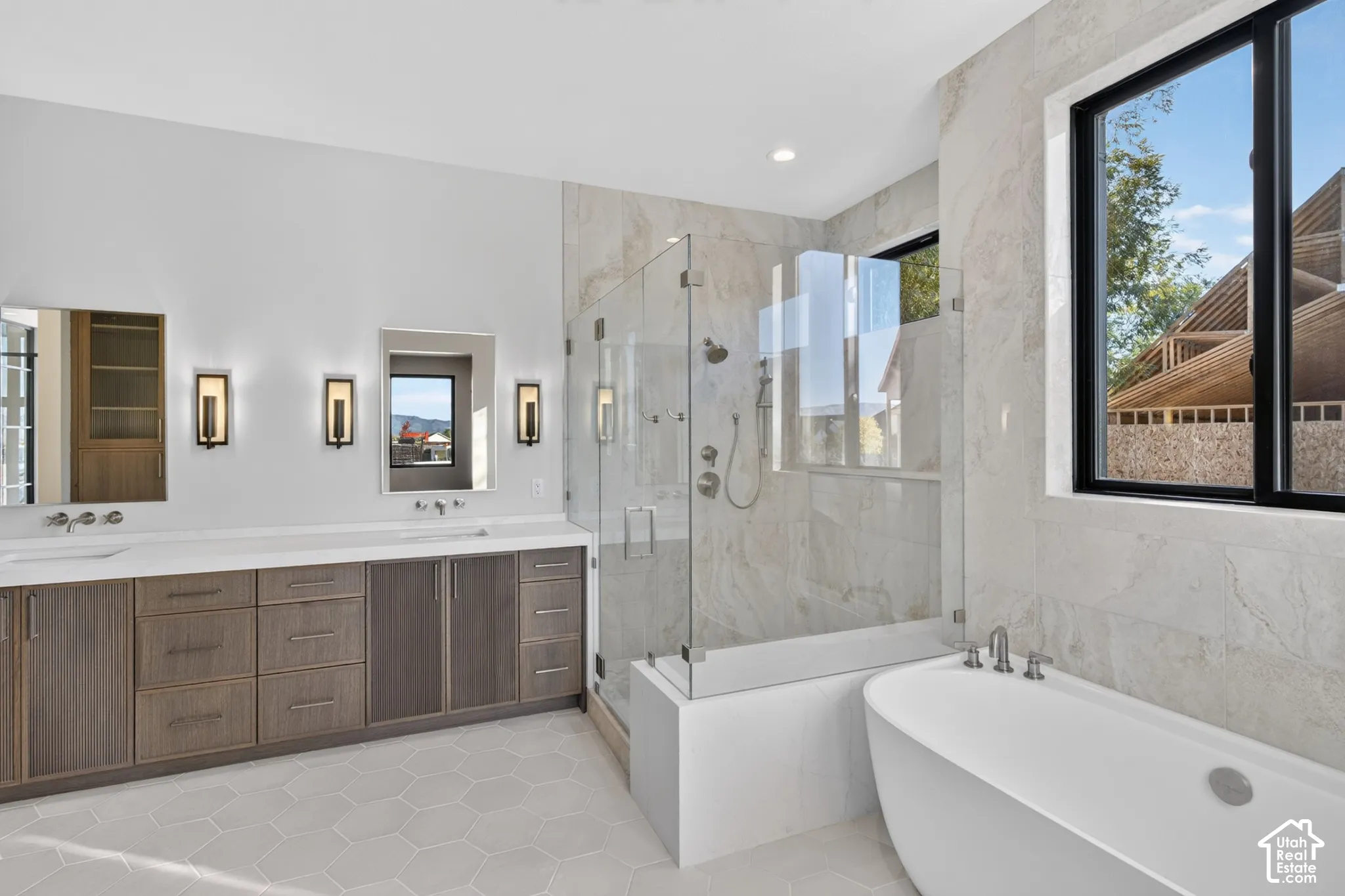 Dual-sink vanity with flat-panel cabinetry and quartz countertop, freestanding soaking tub, walk-in glass-enclosed shower, large-format tile surround, and hexagonal floor tile