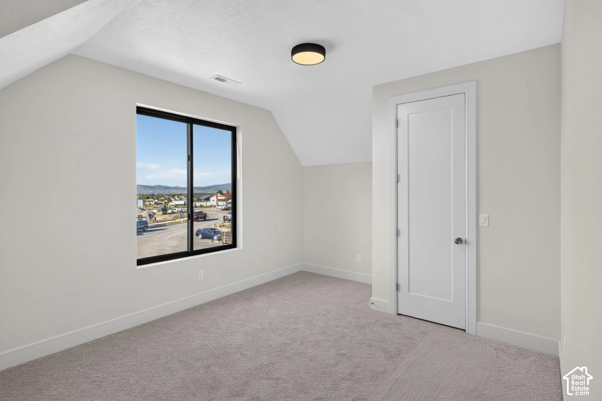 Interior room featuring sloped ceilings, neutral wall tones, wall-to-wall carpeting, a multi-pane window with black trim, and a flush-mount circular lighting fixture