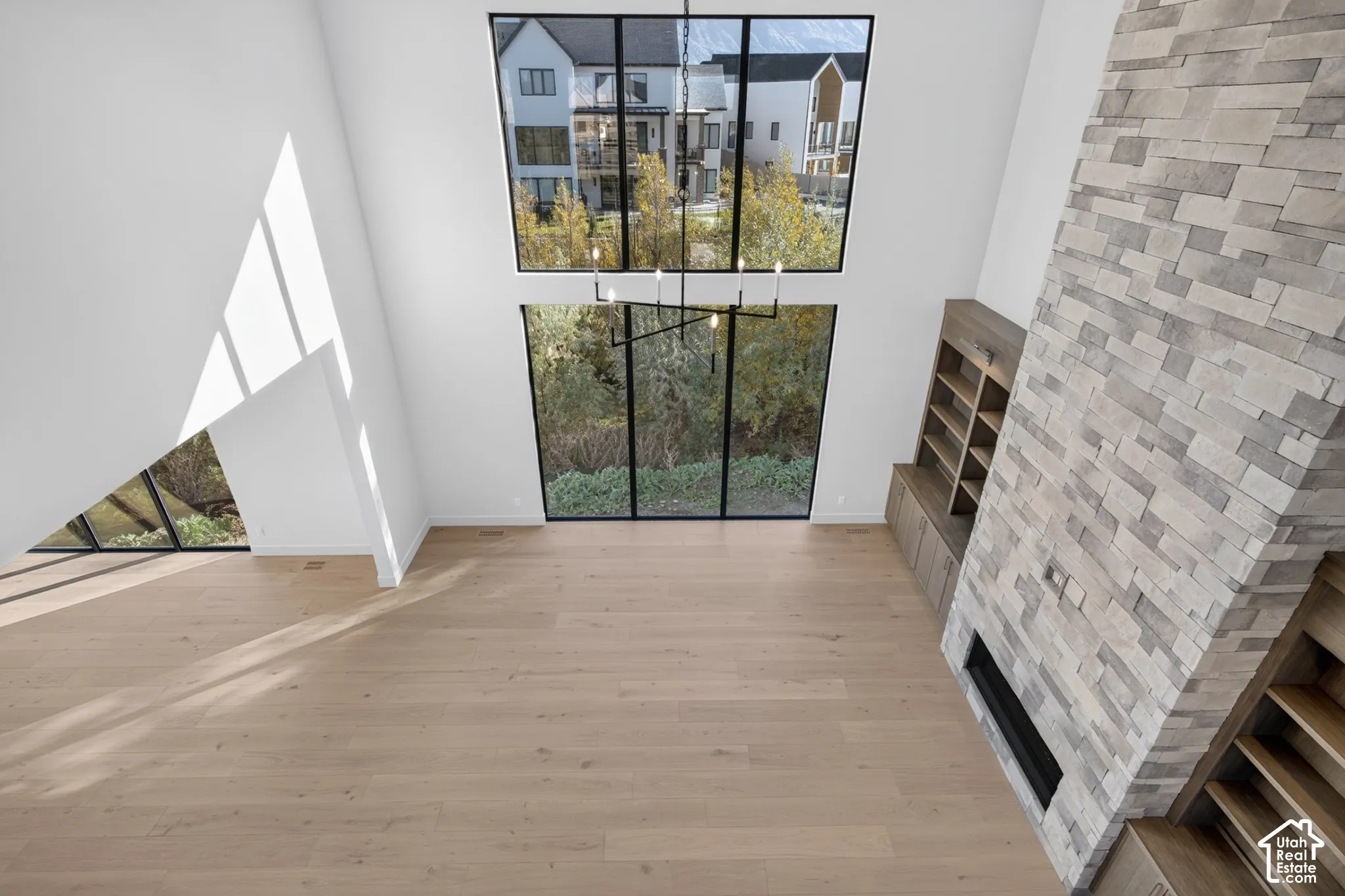Vaulted ceilings featuring floor-to-ceiling windows with black frames, wood-finish flooring, a full-height stone fireplace, and built-in wood shelving