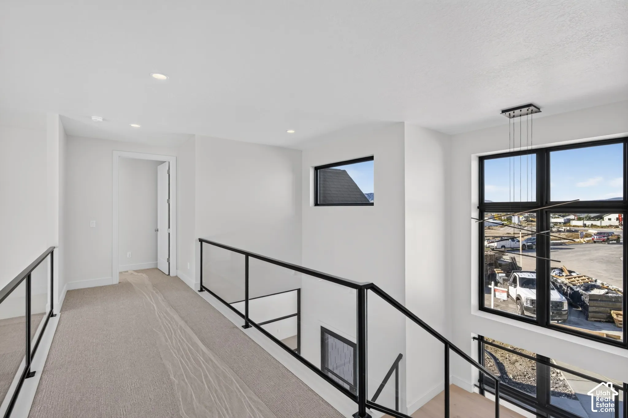 Modern metal railing with glass panels, large picture windows with black frames, recessed ceiling lighting, and neutral carpeting