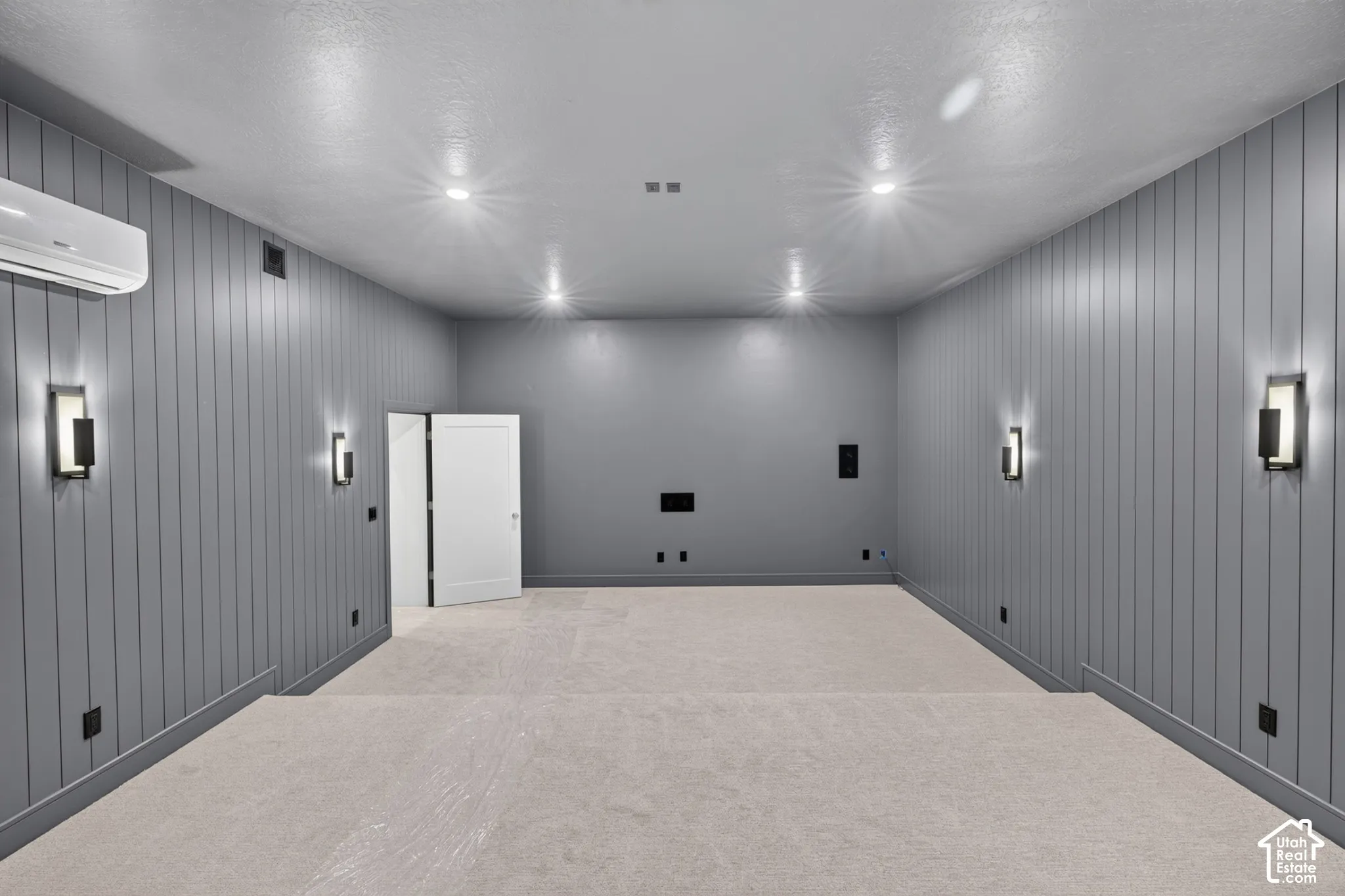 Vertical paneled wall cladding, tiered flooring, recessed ceiling lighting, wall-mounted sconces, and a wall-mounted climate control unit