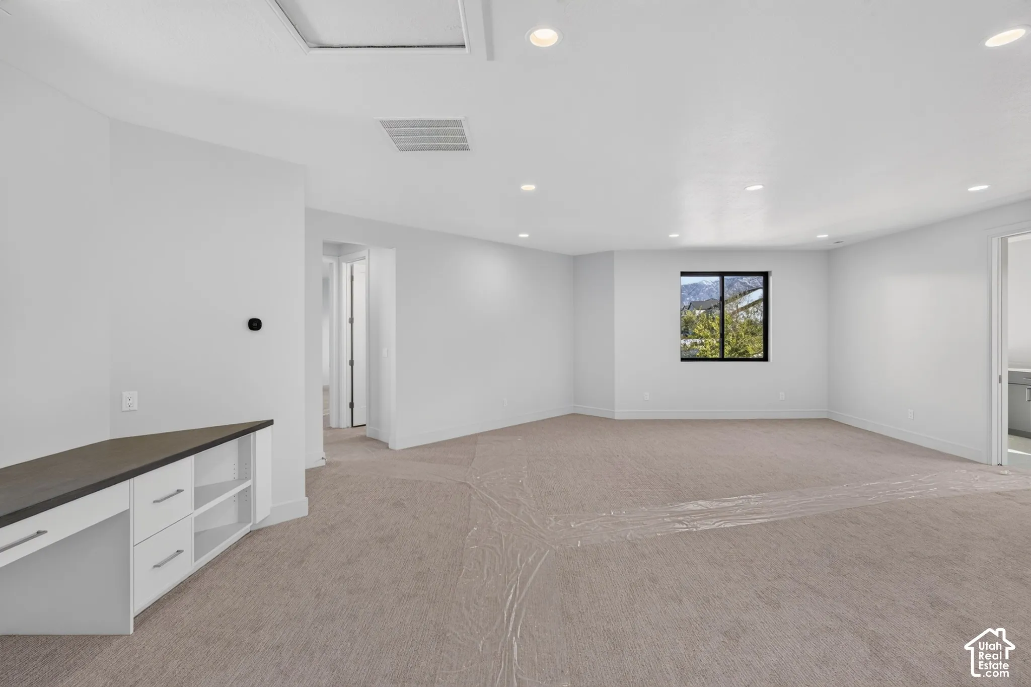 Spacious room featuring neutral carpeting, recessed lighting, built-in cabinetry with a dark surface, and a window with a mountain backdrop