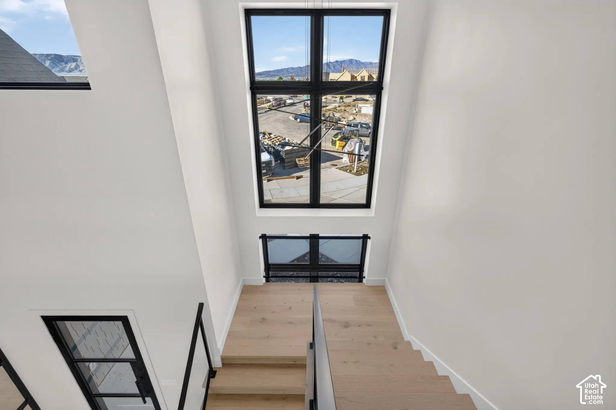 Two-story entryway featuring floor-to-ceiling windows with black frames, wood-finish stairs, and a metal railing with a black finish