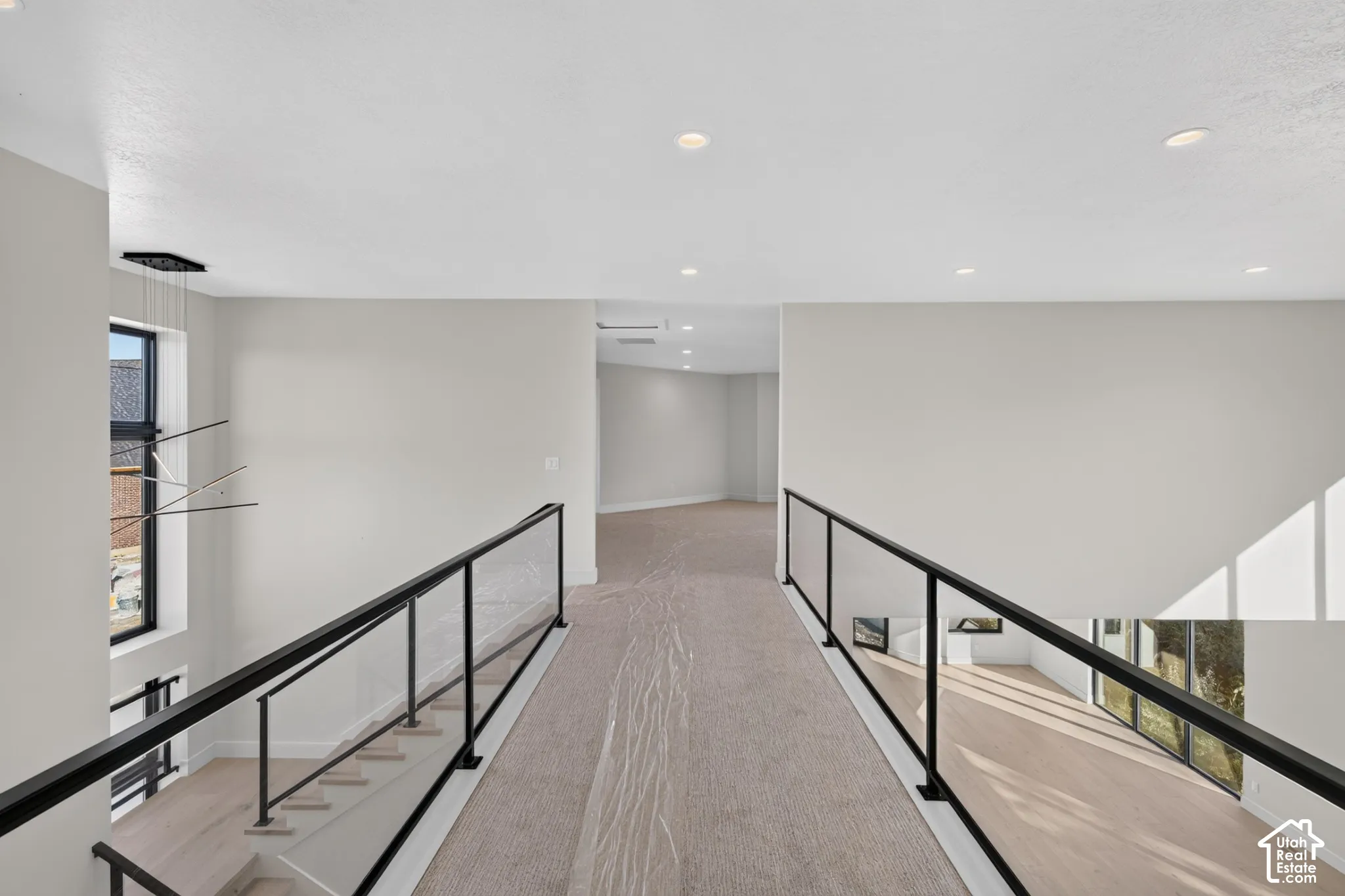 Elevated walkway featuring black metal railings with glass panels, recessed ceiling lighting, and carpeted flooring