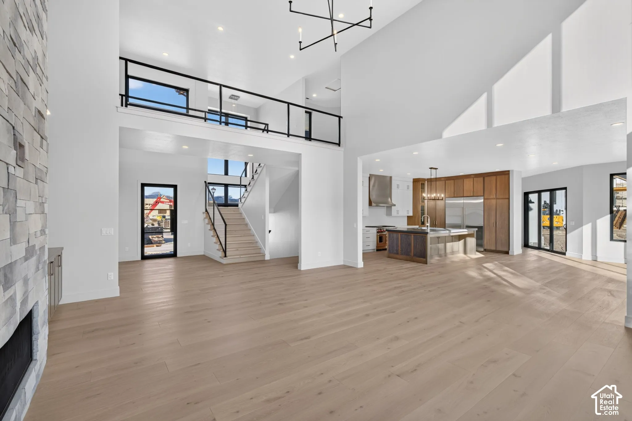 Vaulted ceilings with stacked-stone floor-to-ceiling fireplace, wood-finish flooring, metal staircase railing, lofted gallery, and kitchen featuring custom cabinetry with center island