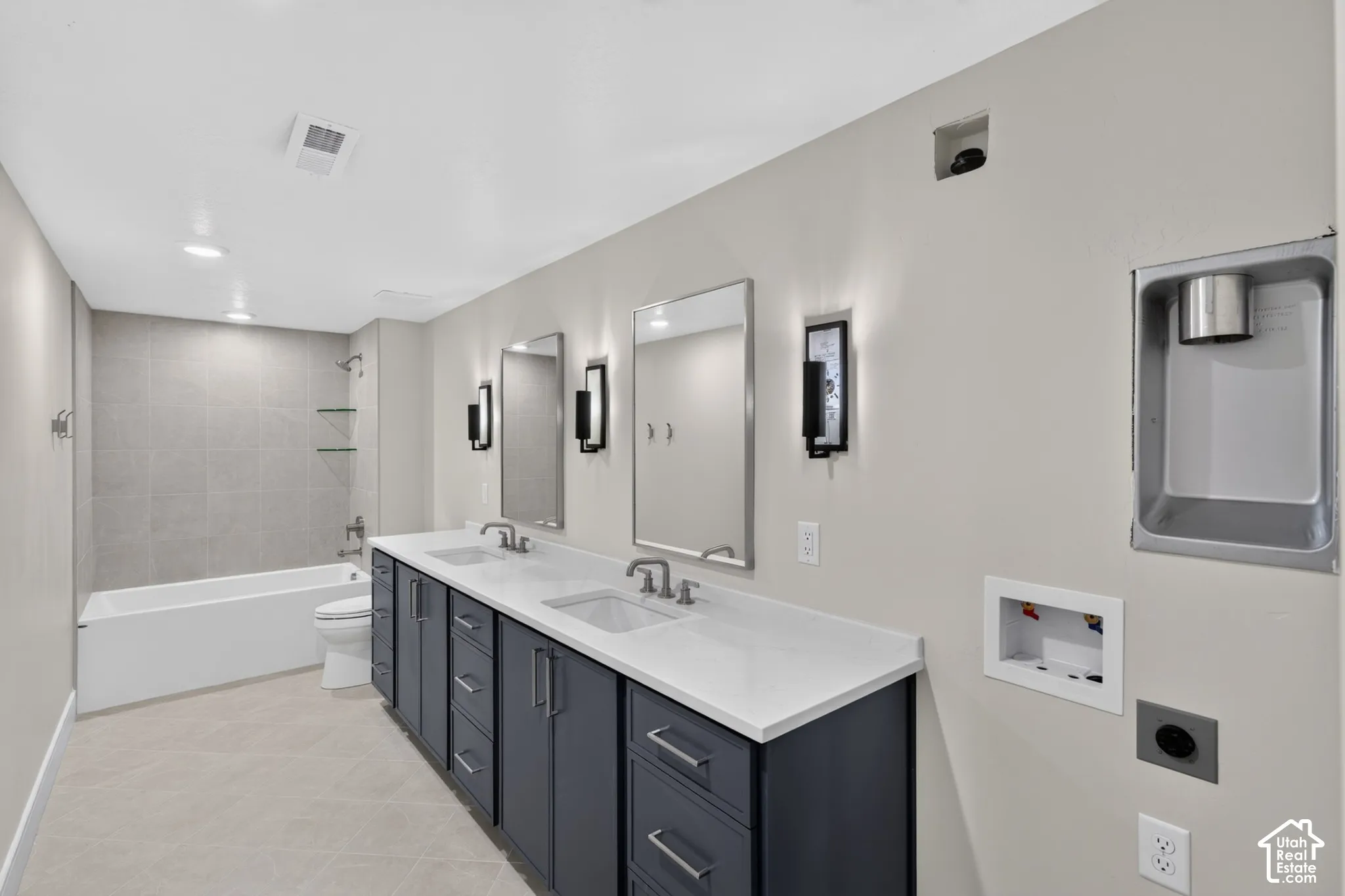 Dual-sink vanity with dark cabinetry, quartz countertop, and rectangular undermount sinks, complemented by a tiled bathtub surround and wall-mounted light fixtures
