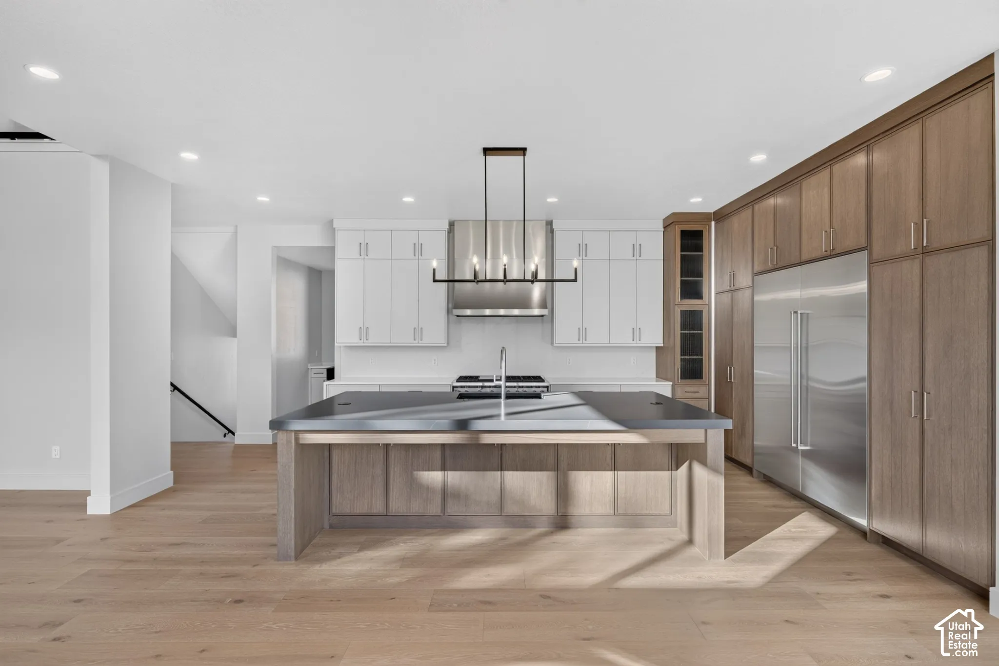 Kitchen featuring wood-finish cabinetry, central island with a solid surface countertop, stainless steel appliance suite, linear chandelier, and wood-finish flooring