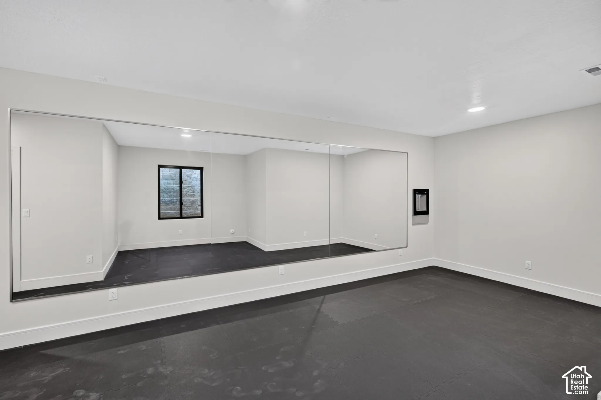 Full-wall mirror, recessed lighting, matte black-framed window, and dark flooring