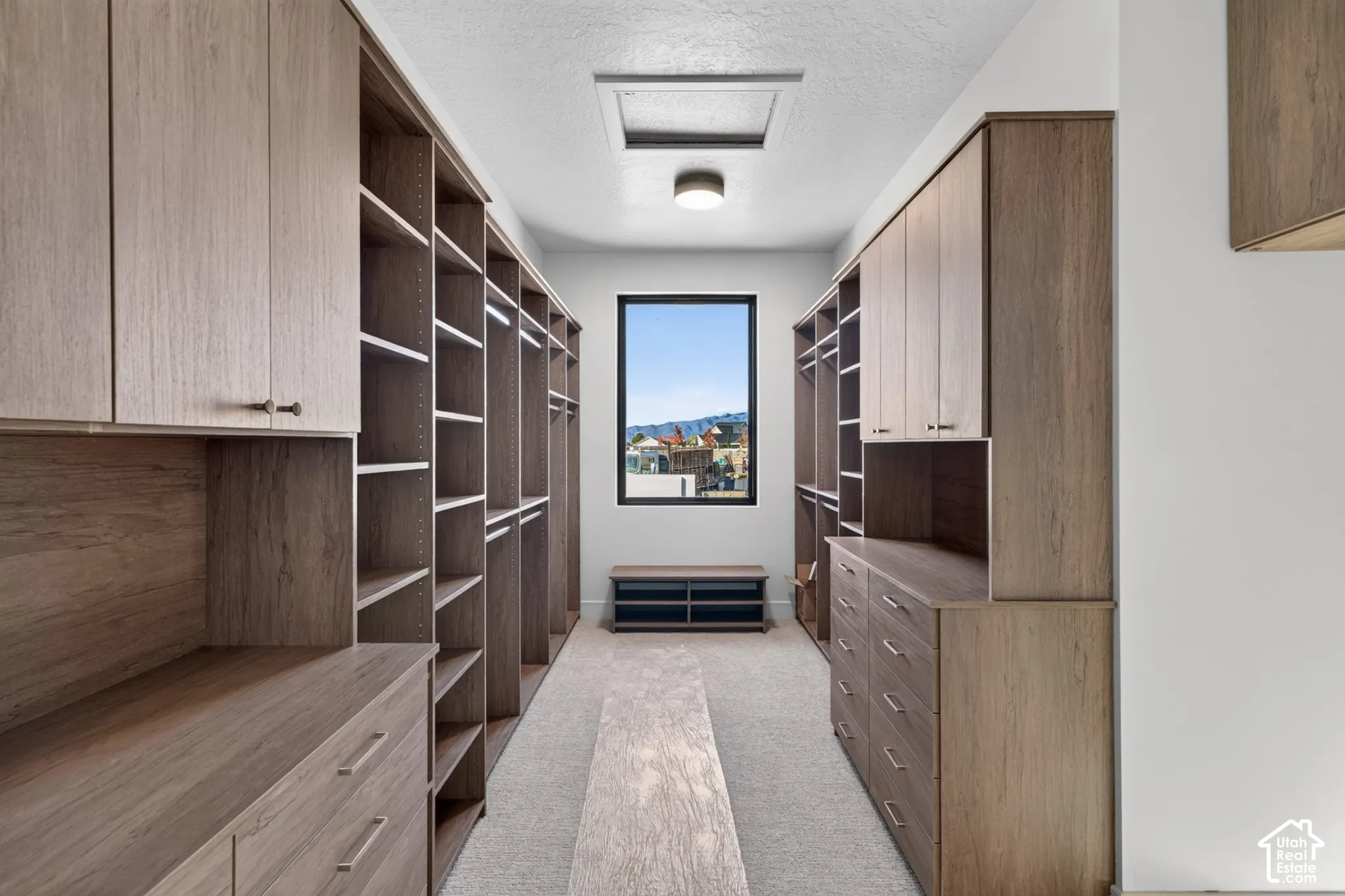 Custom walk-in closet featuring extensive wood-finish cabinetry, built-in shelving, integrated dresser drawers, and a central window with exterior scenery