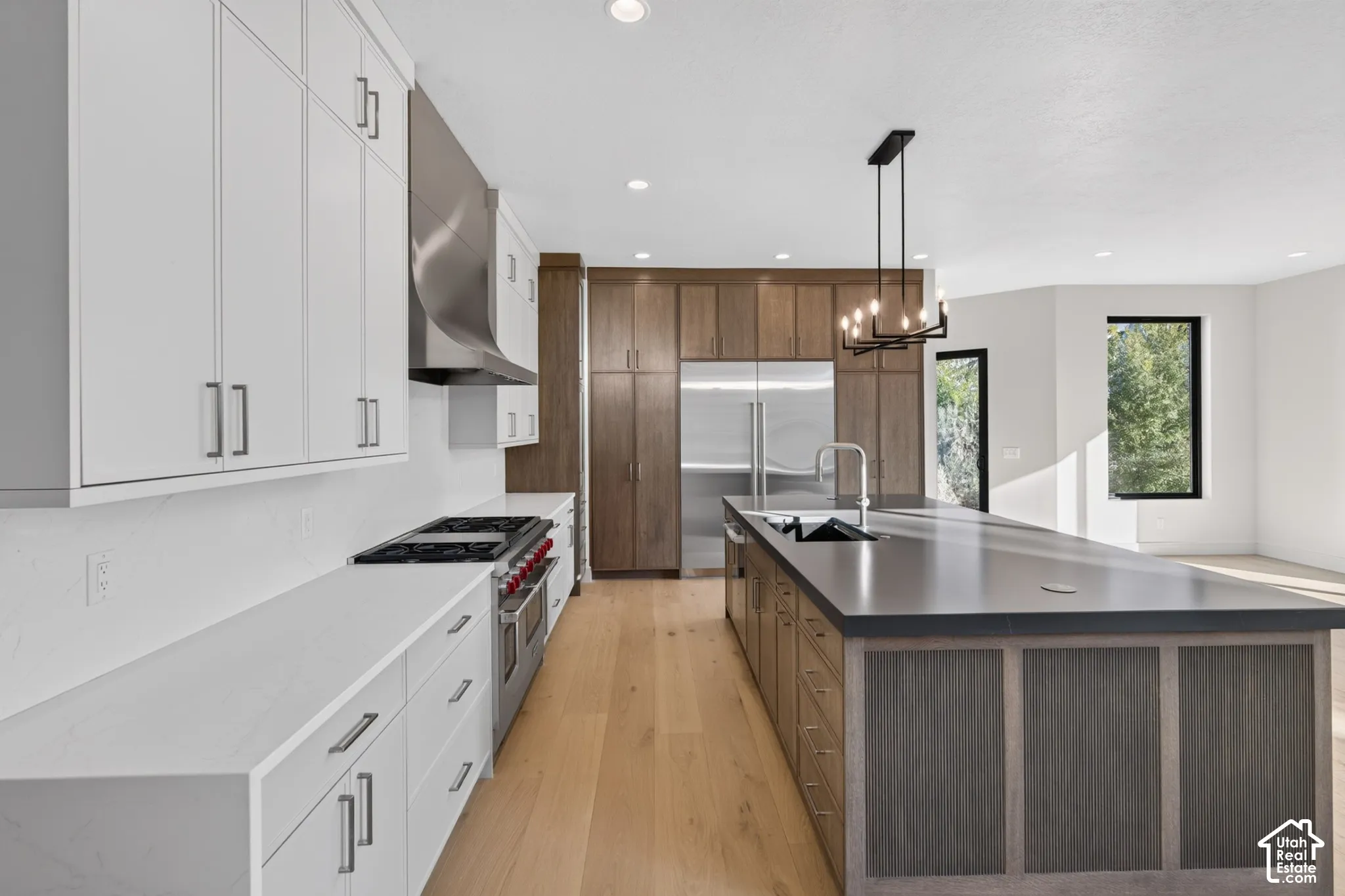 Kitchen featuring two-tone cabinetry, wood-finish flooring, a large island with a dark countertop, a stainless steel range with a professional-style vent hood, and recessed lighting