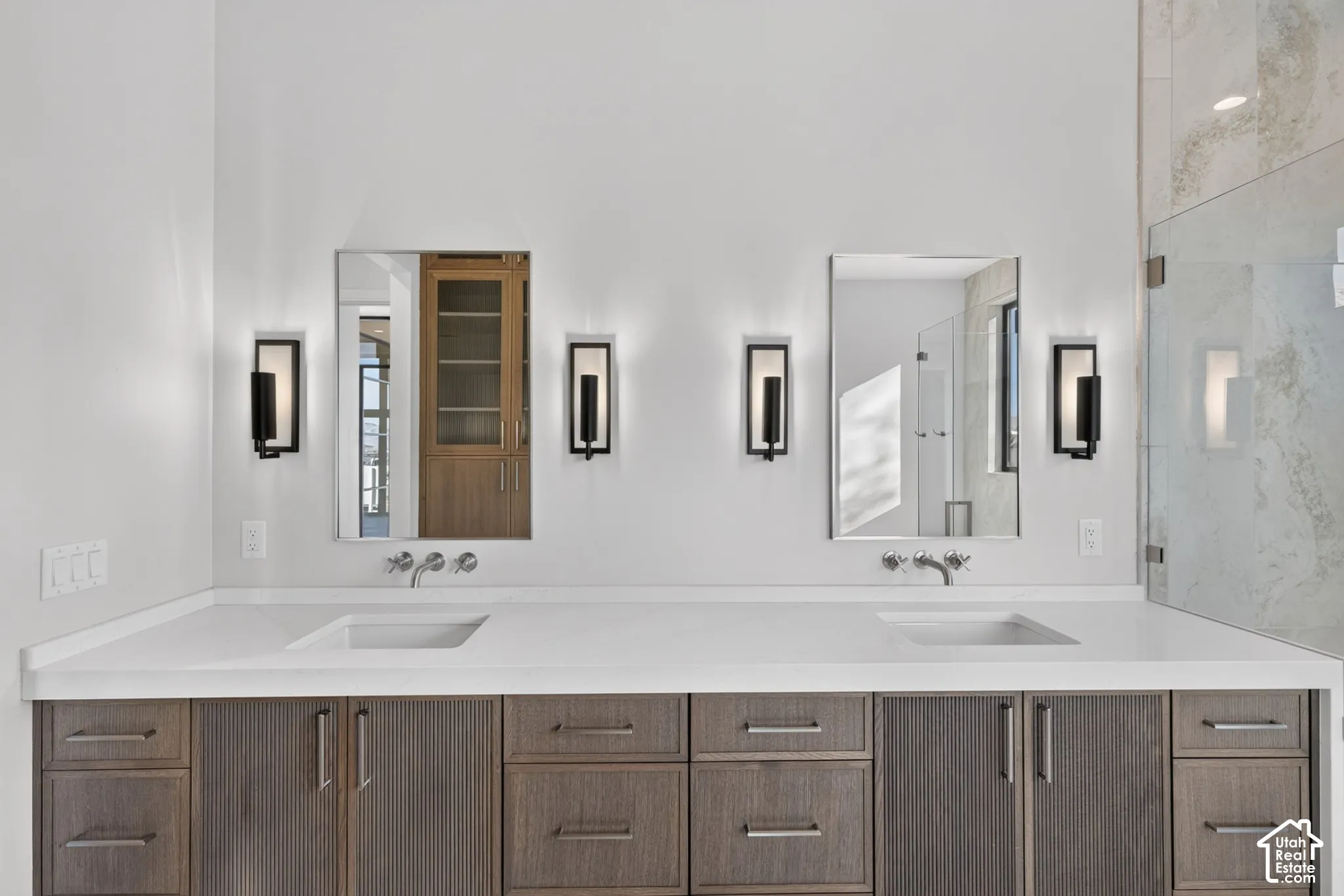 Dual-sink vanity featuring wood-finish cabinetry, white countertop, wall-mounted faucets, rectangular mirrors, and four wall-mounted sconces