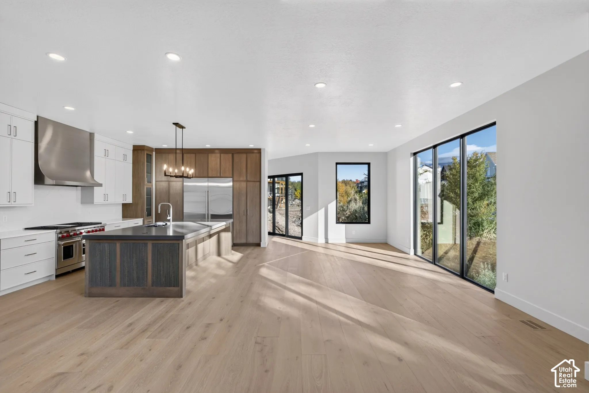 Kitchen featuring two-tone cabinetry, a professional-grade stainless steel range hood, an oversized center island, wood-finish flooring, and expansive floor-to-ceiling windows