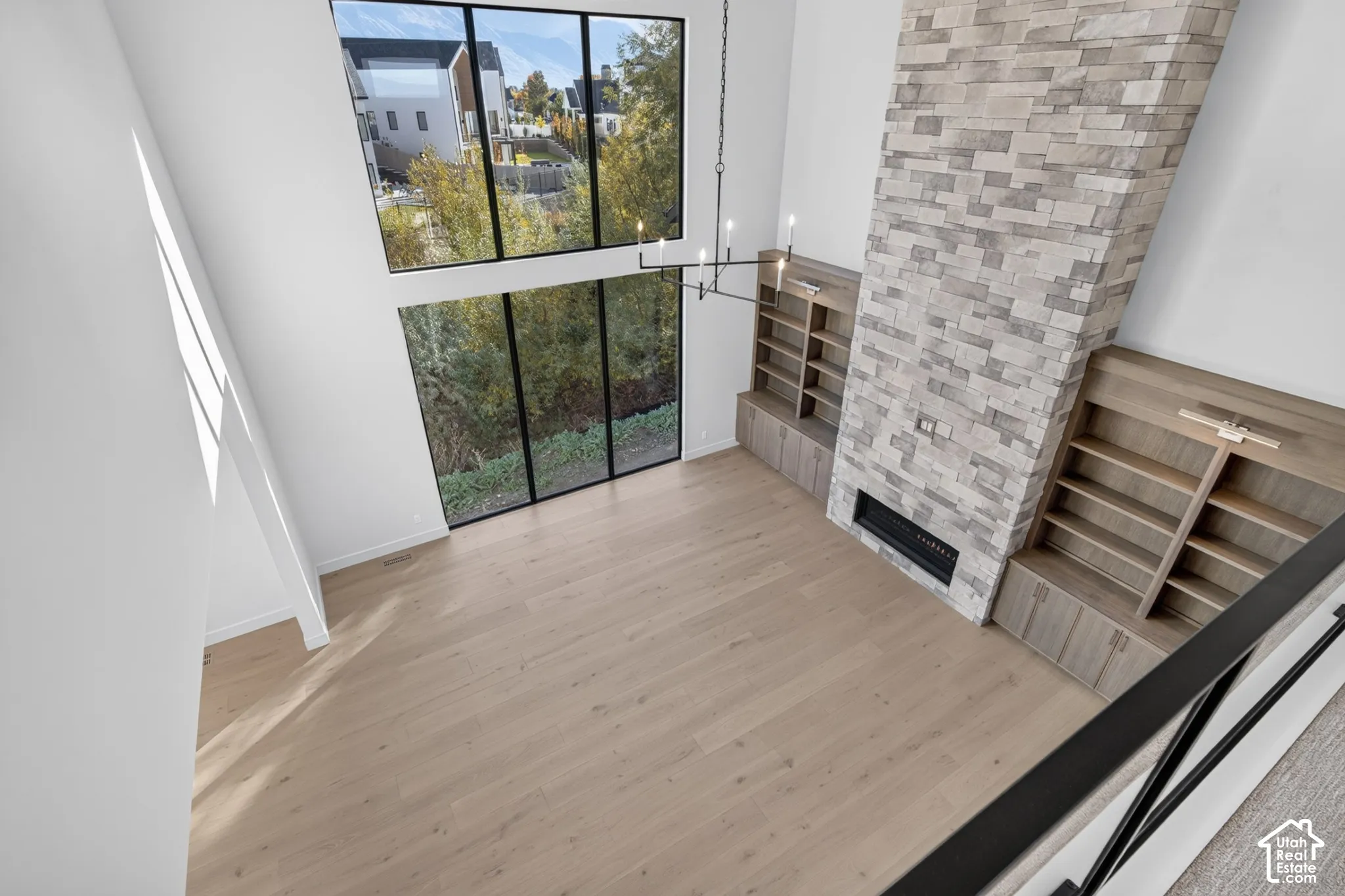 Double-height space featuring floor-to-ceiling windows, stacked-stone fireplace, built-in wooden cabinetry, and wood-finish flooring