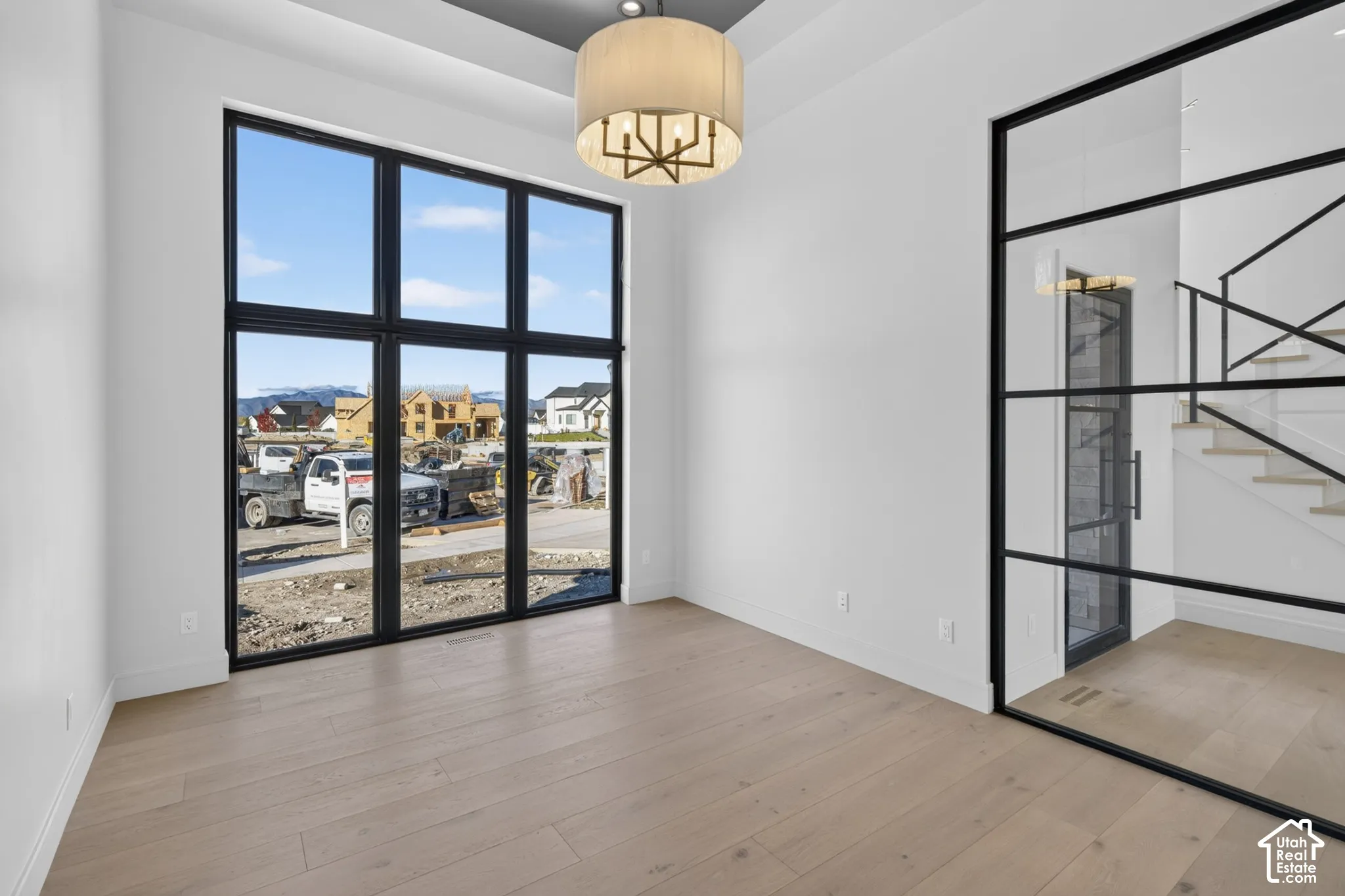 Floor-to-ceiling black-framed windows, wood-finish flooring, tray ceiling with recessed lighting, drum pendant fixture, and glass-paneled metal partition wall
