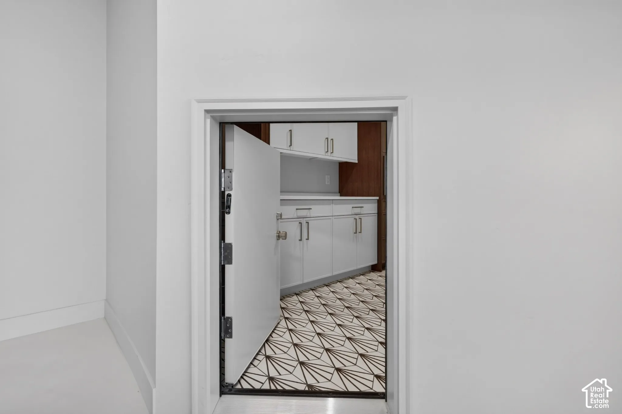 Reinforced steel door featuring heavy-duty hinges, geometric patterned flooring, white cabinetry with silver-tone pulls, and solid-surface countertops