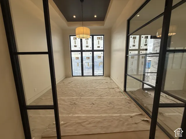 Enclosed space featuring floor-to-ceiling black metal-framed glass doors, a recessed tray ceiling with dark finish, and a central drum pendant light