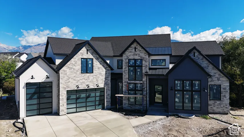 Multi-gabled exterior featuring stone veneer, vertical siding, metal roofing accents, multi-pane windows, and frosted glass garage doors