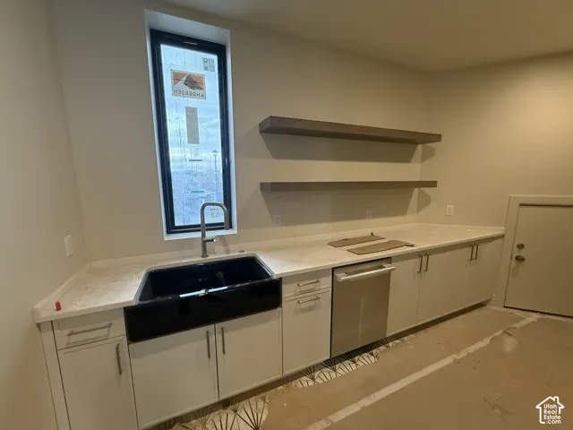 Kitchen featuring white cabinetry, quartz countertops, a black farmhouse-style sink with a gooseneck faucet, integrated stainless steel dishwasher, and dual floating shelves