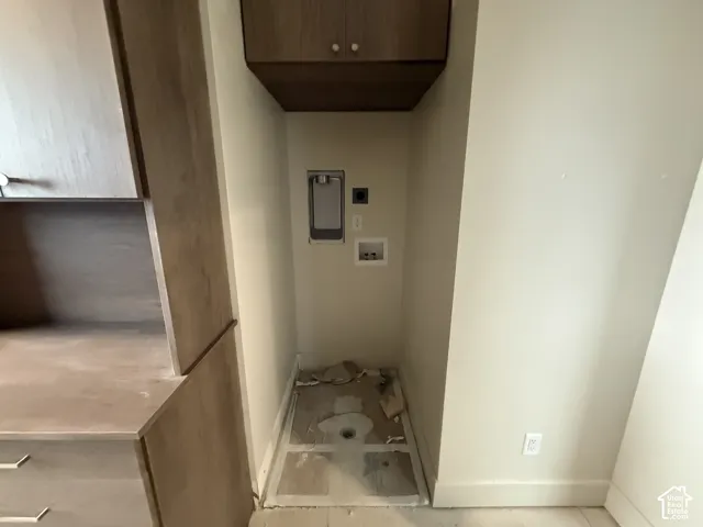 Utility alcove featuring built-in wood-finish cabinetry, upper storage cupboard, and dedicated water and electrical hookups
