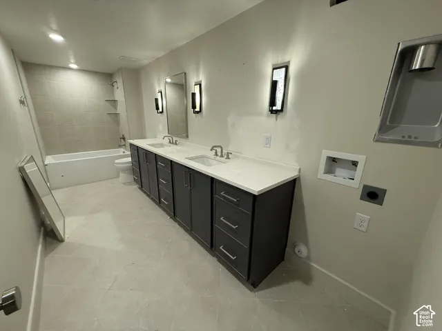 Double vanity featuring dark cabinetry, rectangular undermount sinks, light-toned stone-finish countertops, and vertical wall-mounted lighting