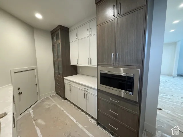 Custom cabinetry featuring dark-stained wood-finish towers, white shaker-style cabinetry, a solid-surface countertop, and a built-in stainless steel microwave