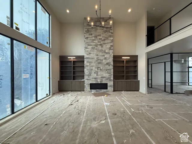 Floor-to-ceiling windows, full-height stone fireplace surround, custom built-in cabinetry, modern chandelier, and minimalist metal-framed interior partitions