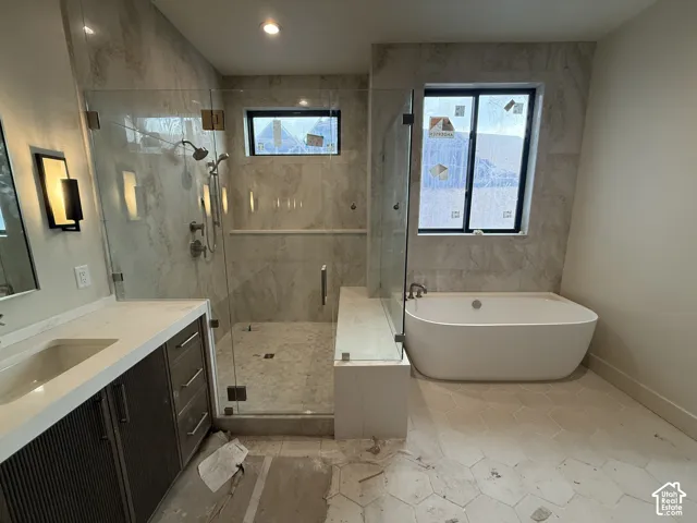 Bathroom featuring a walk-in shower with glass enclosure, freestanding soaking tub, stone-finish wall tile, hexagonal floor tile, and a custom vanity with a solid-surface countertop