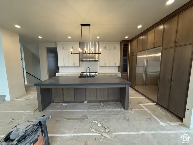 Kitchen featuring a large central island with a solid surface countertop, stainless steel refrigerator, professional-grade range, linear chandelier, and custom ceiling-height cabinetry