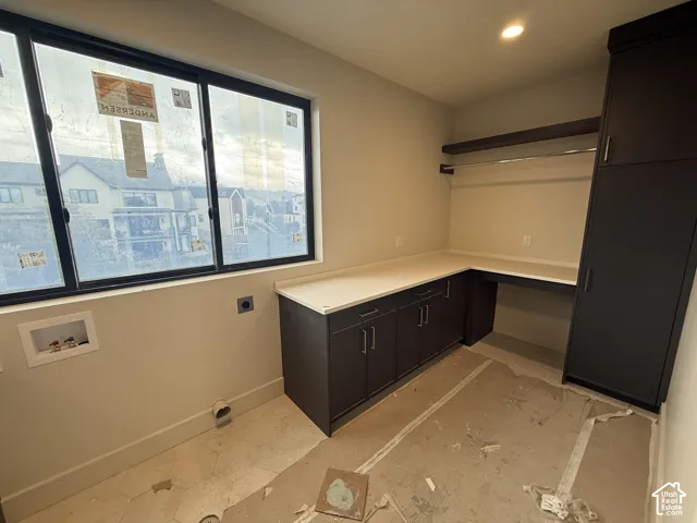 Utility room featuring dark-finish cabinetry, light-toned stone-style countertops, an integrated tall storage cabinet, and a multi-pane window
