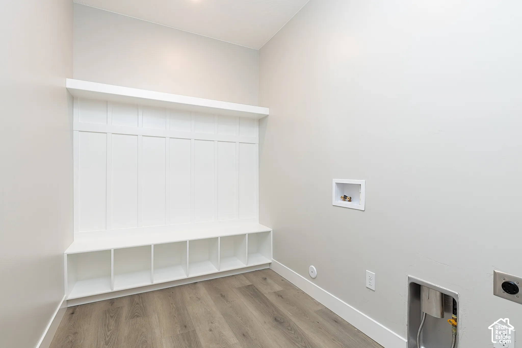 Built-in white wood storage cubbies featuring upper shelving and vertical paneling detail, complemented by wood-finish flooring