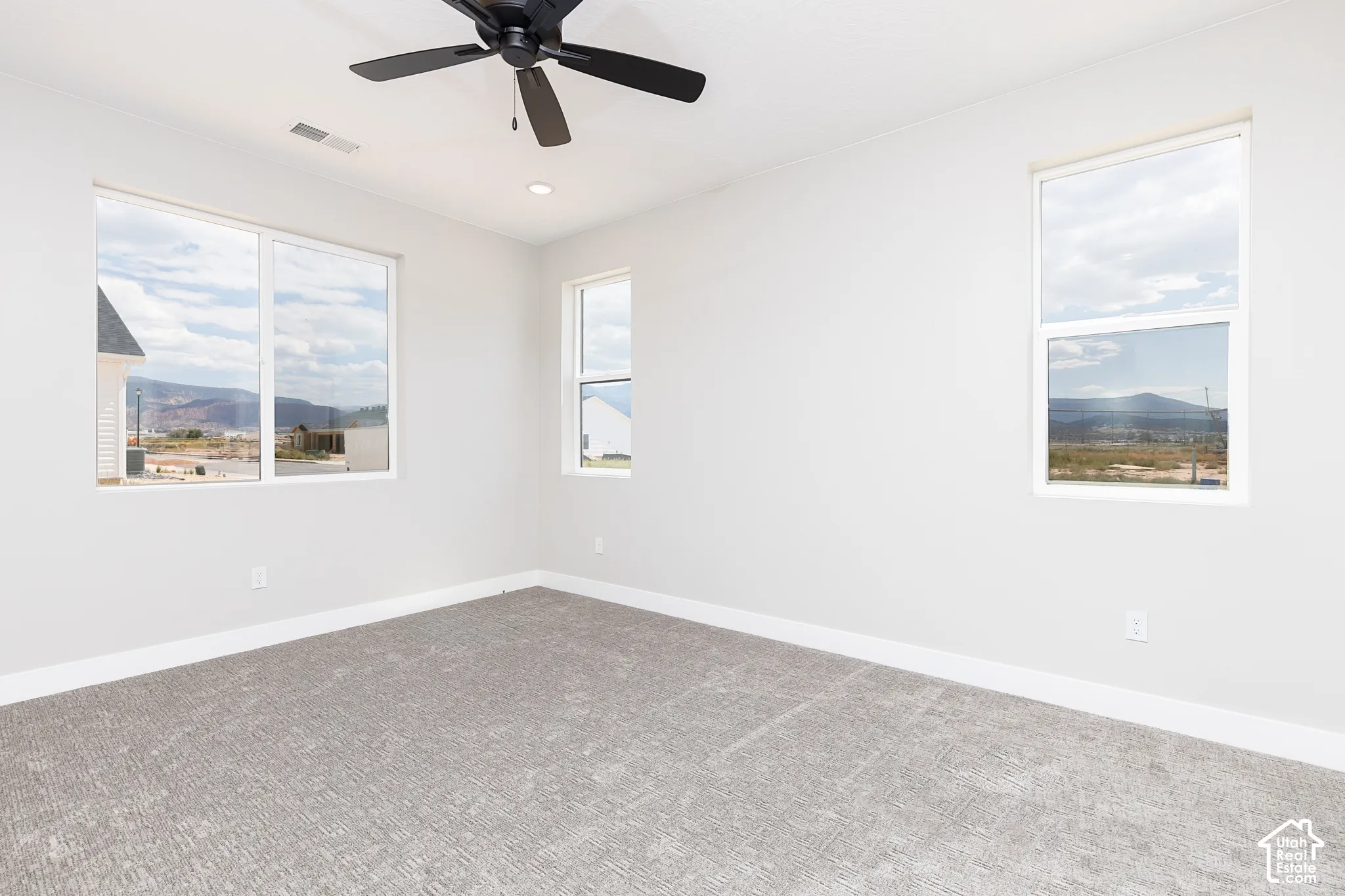 Interior room featuring neutral wall tones, plush wall-to-wall carpeting, a matte black ceiling fan, recessed lighting, and multiple windows with mountain scenery