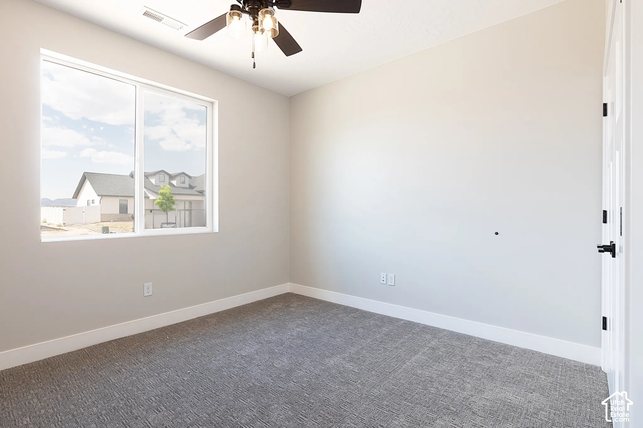 Neutral interior space featuring carpeted flooring, a large single-pane window, and a ceiling fan with integrated lighting