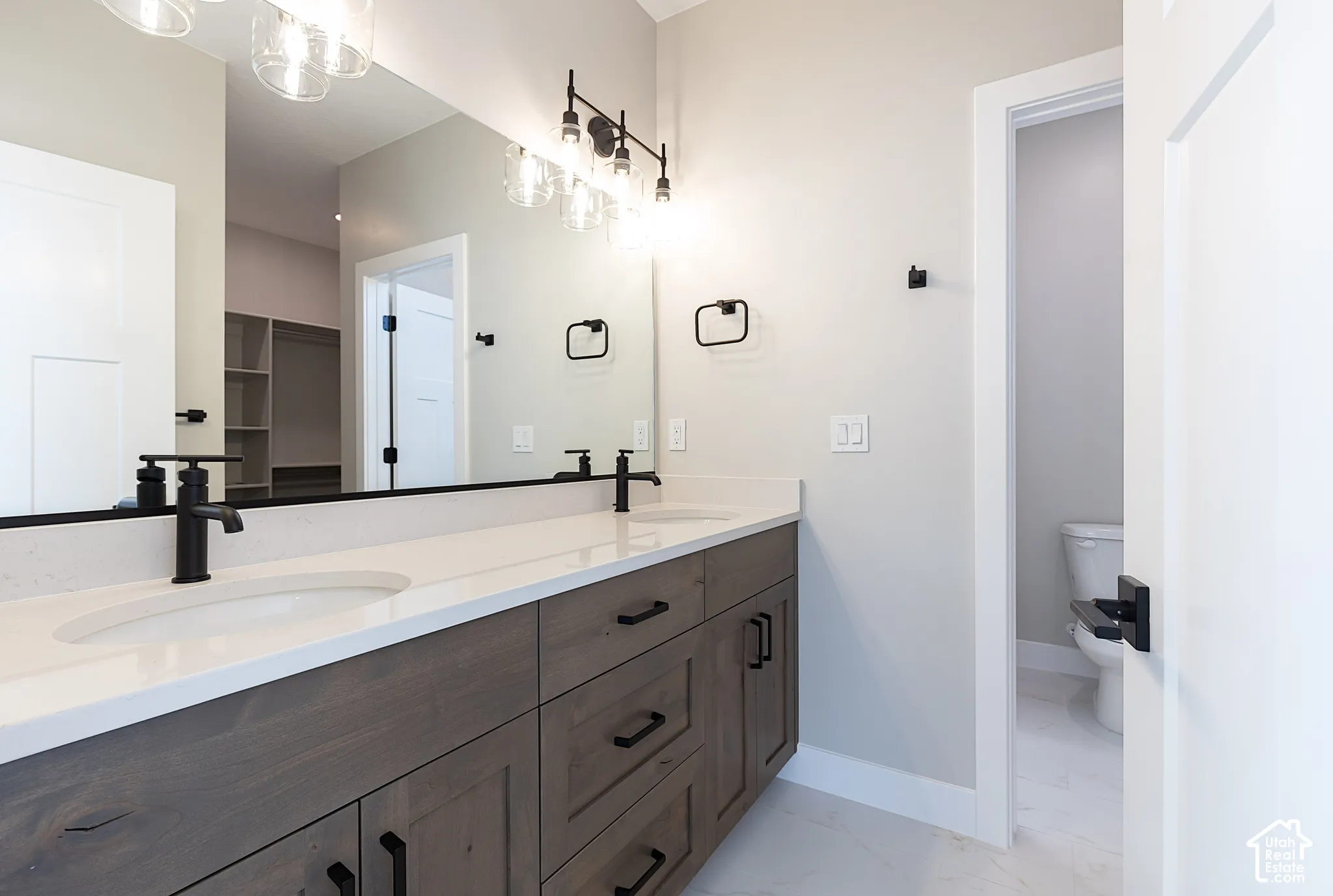 Dual-sink vanity with stained wood cabinetry, quartz countertop, matte black fixtures, and large rectangular mirror